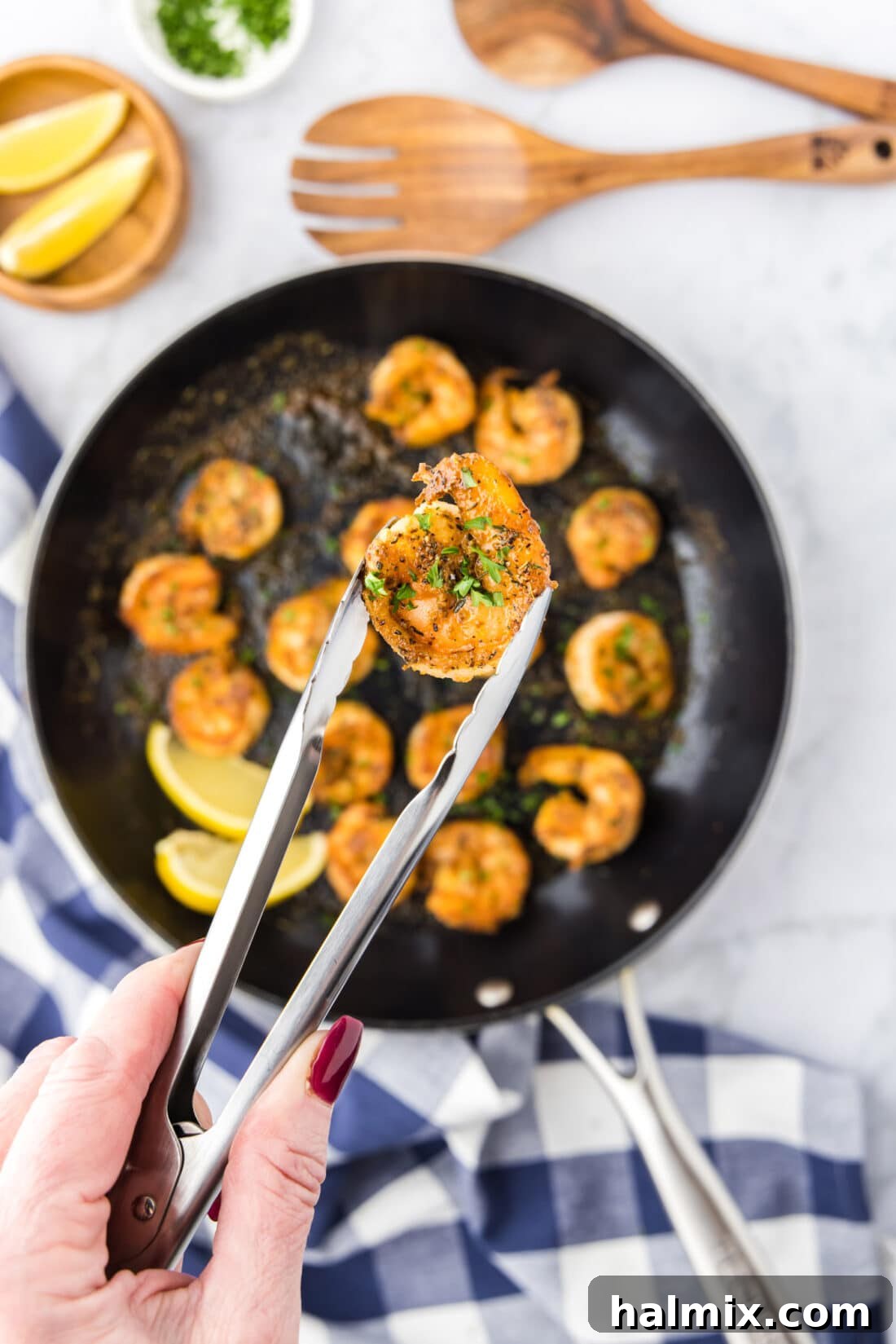Tongs holding a single Cajun shrimp, highlighting its perfect cook and inviting spice coating.