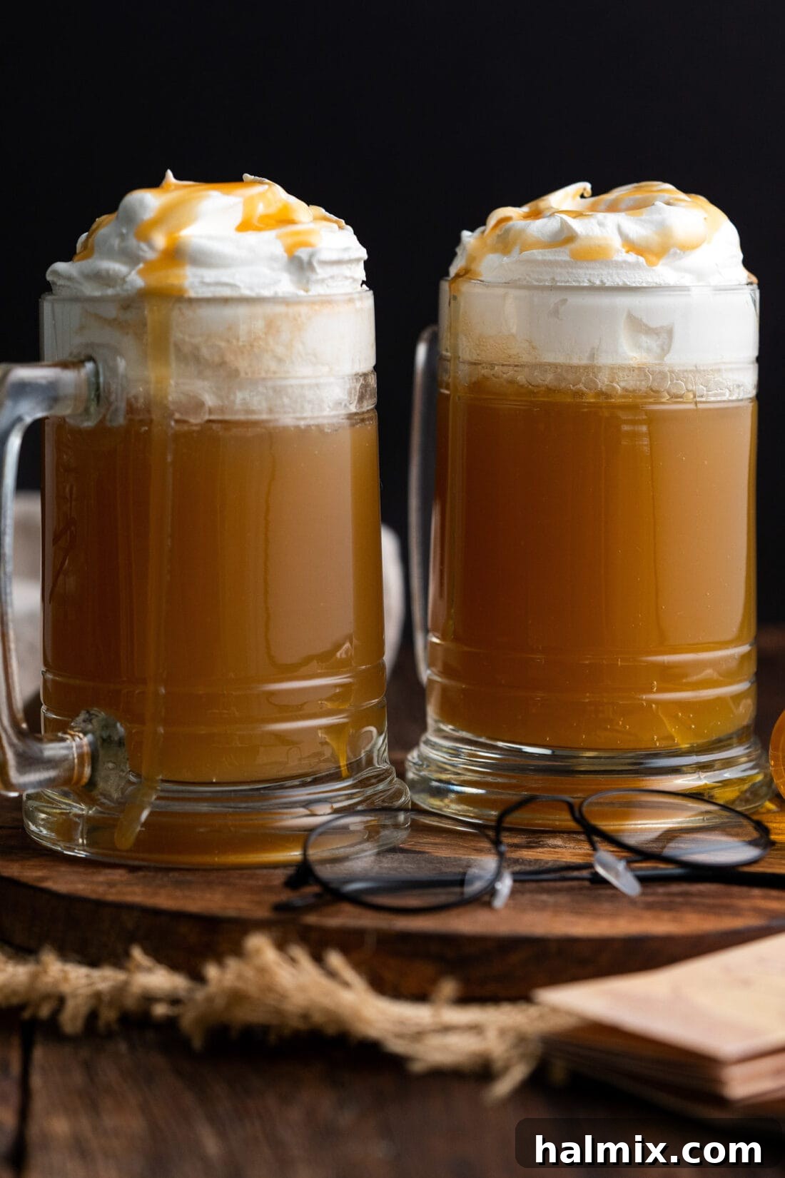 Two glasses of Butterbeer, beautifully topped with whipped cream and a delicate drizzle of butterscotch syrup, ready for a magical moment.