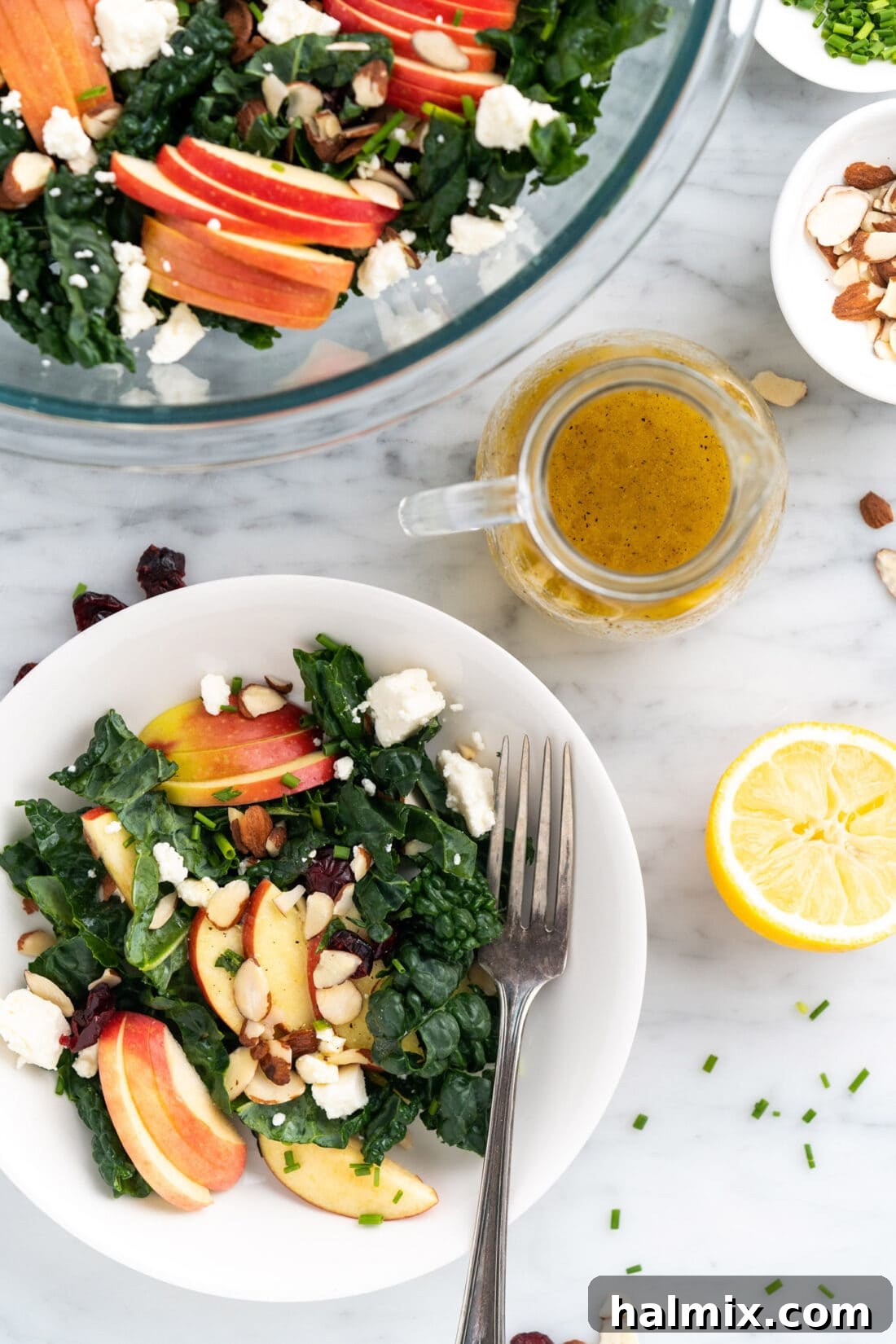 Lemon Salad Dressing in a dressing container surrounded by a plate an bowl of Kale Salad