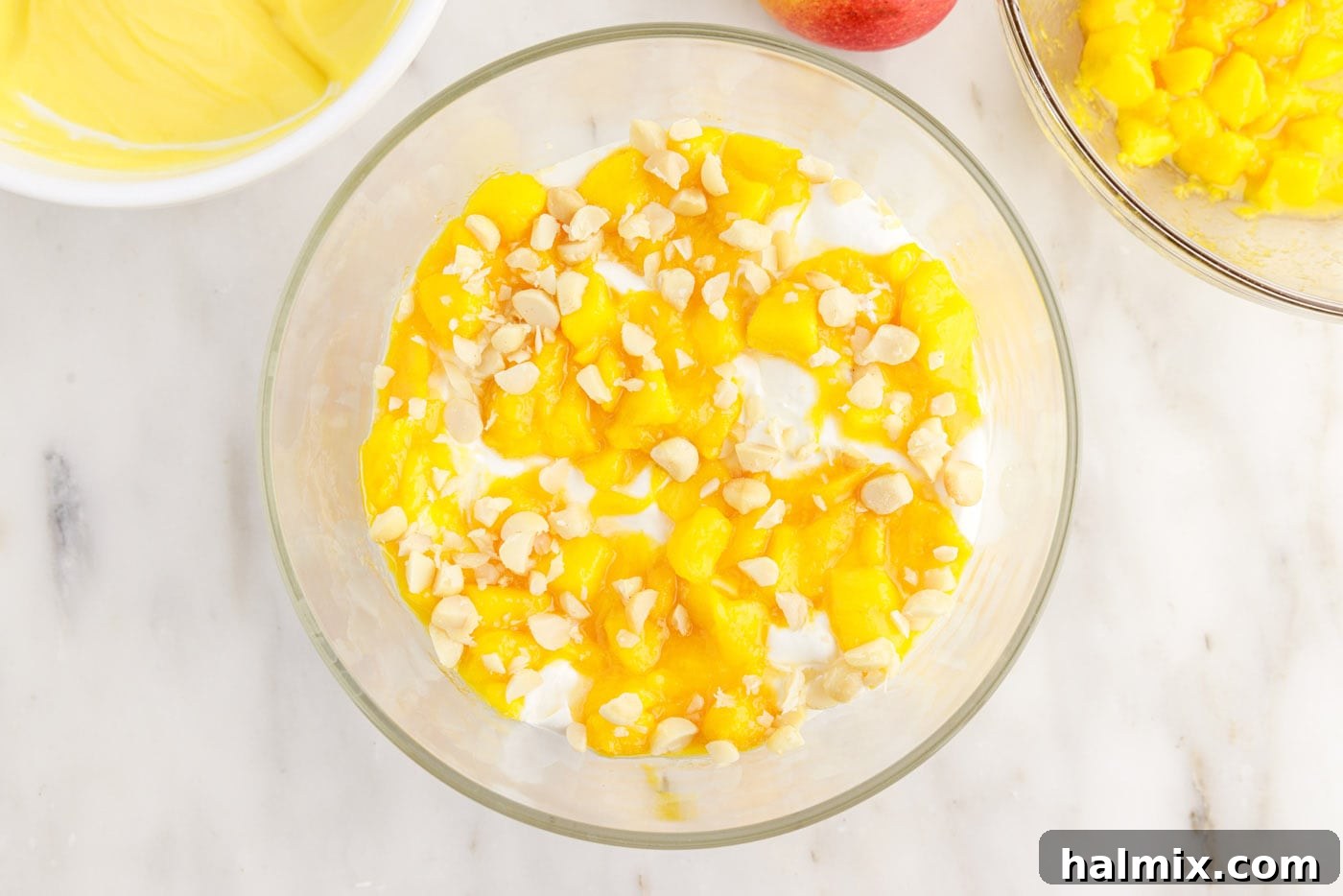 Macadamia nuts sprinkled over mangoes, pudding, whipped cream, and angel food cake in a trifle