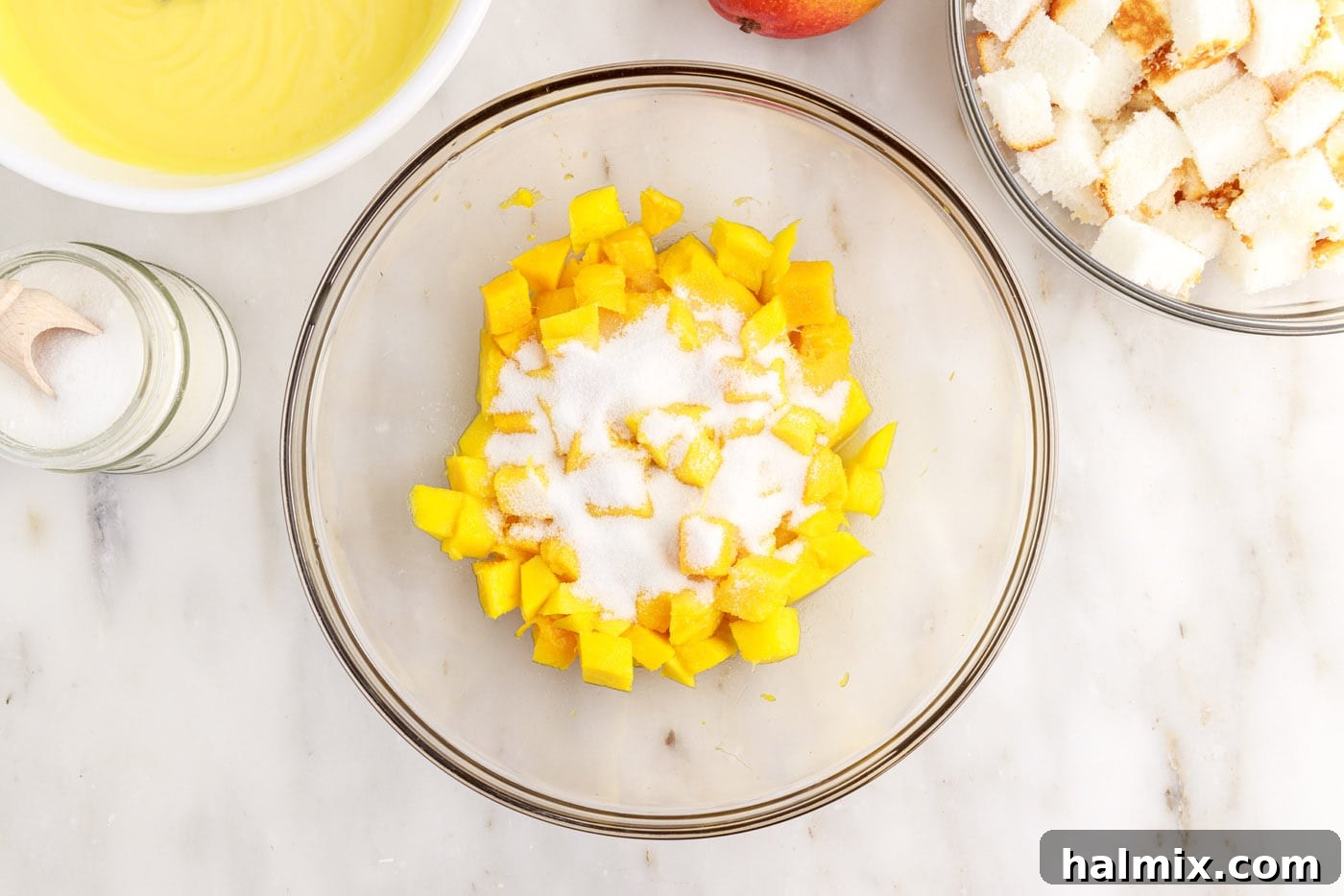 Adding granulated sugar to diced mangoes in a bowl