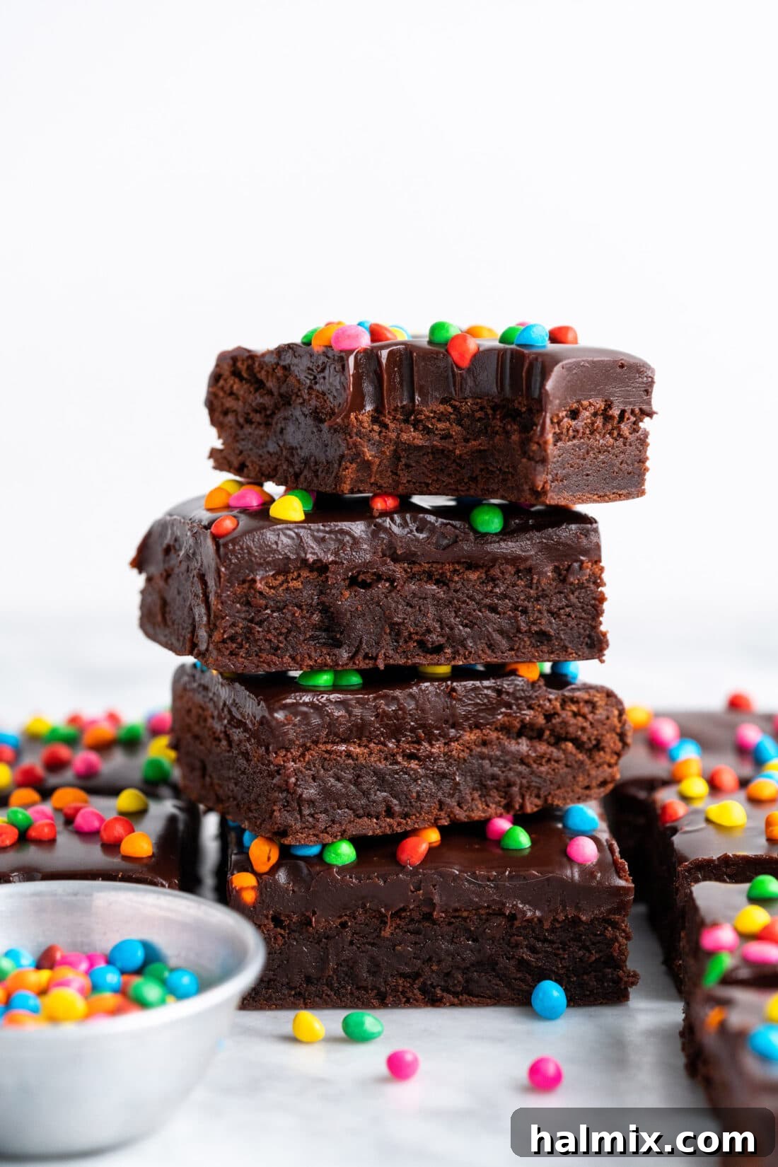 Stack of Homemade Cosmic Brownies with one bite taken out of the top brownie, showcasing the rich ganache and colorful sprinkles.