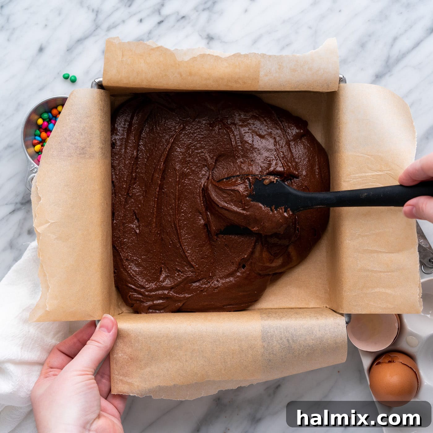 spreading brownie batter evenly in a parchment-lined baking pan
