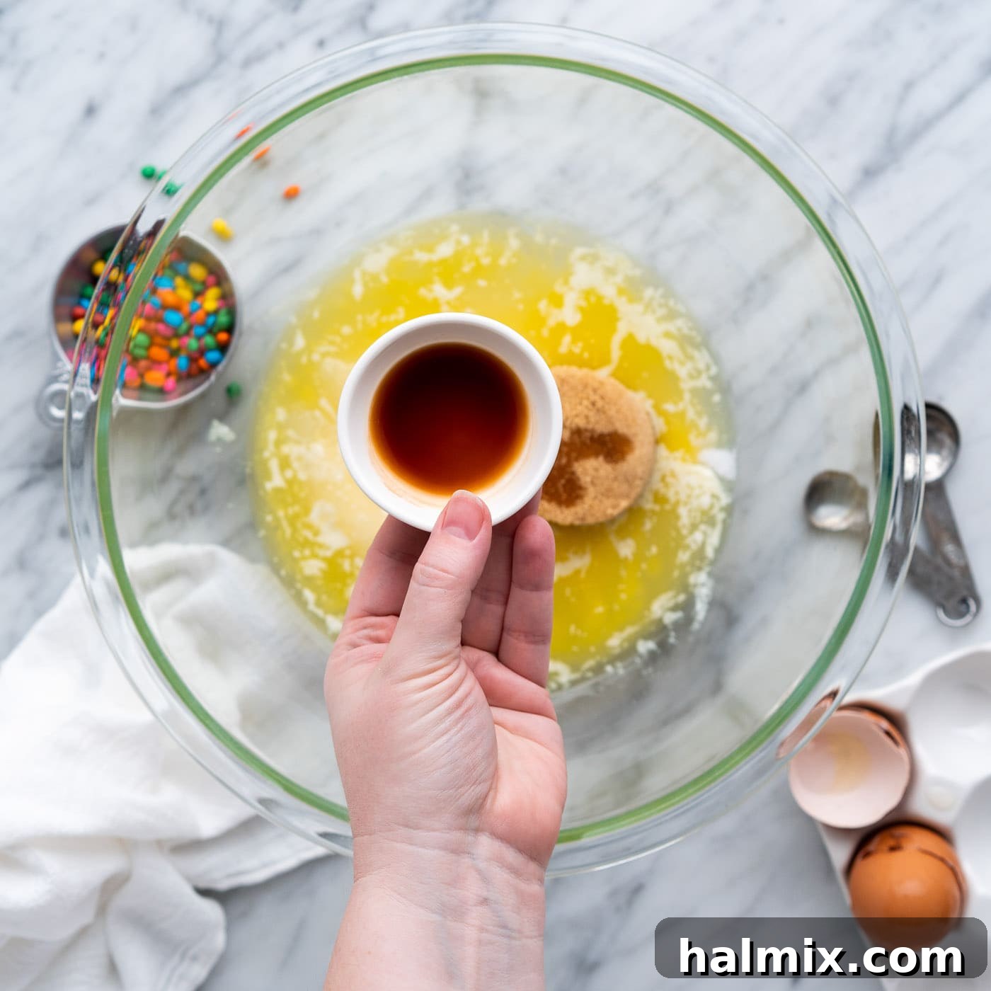 vanilla extract being poured over sugar, oil, and butter mixture in a large bowl
