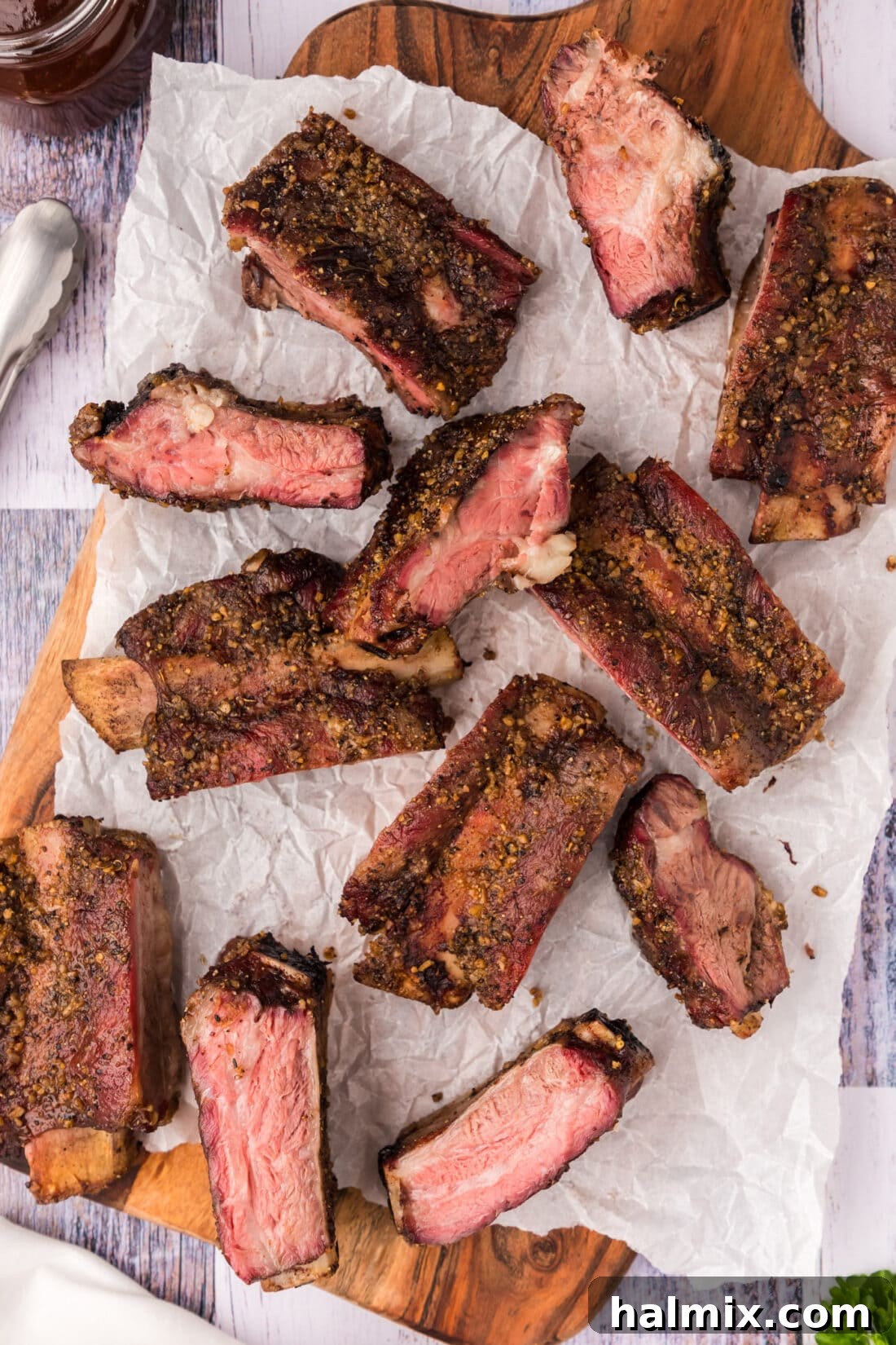Fall-Off-The-Bone Smoked Beef Ribs 2 Smoked Beef Ribs resting on a wooden platter covered in parchment paper, showcasing their rich color and tender texture.