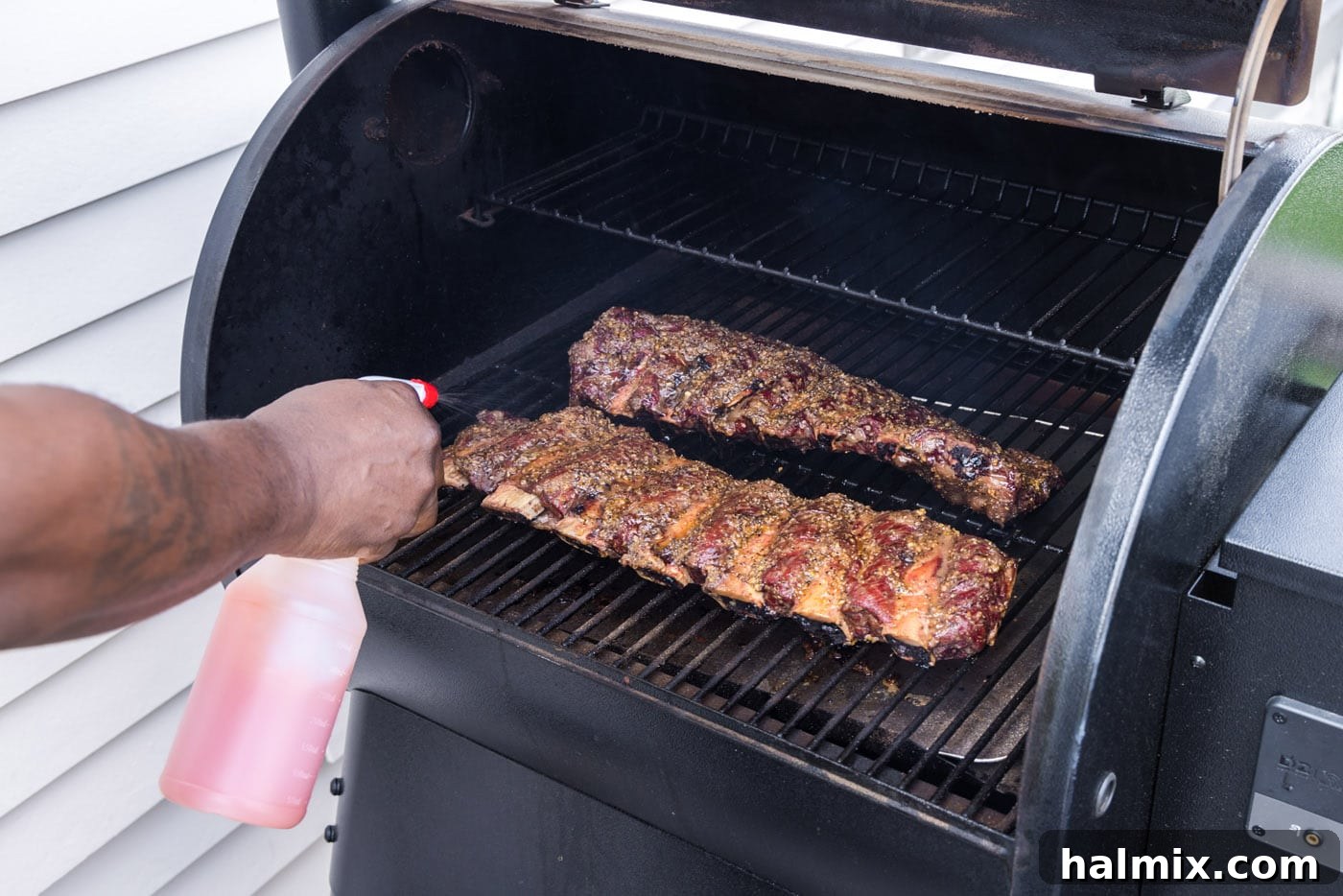 Fall-Off-The-Bone Smoked Beef Ribs 7 A hand spraying beef ribs with an apple cider vinegar mixture on the smoker, ensuring moisture and bark development.