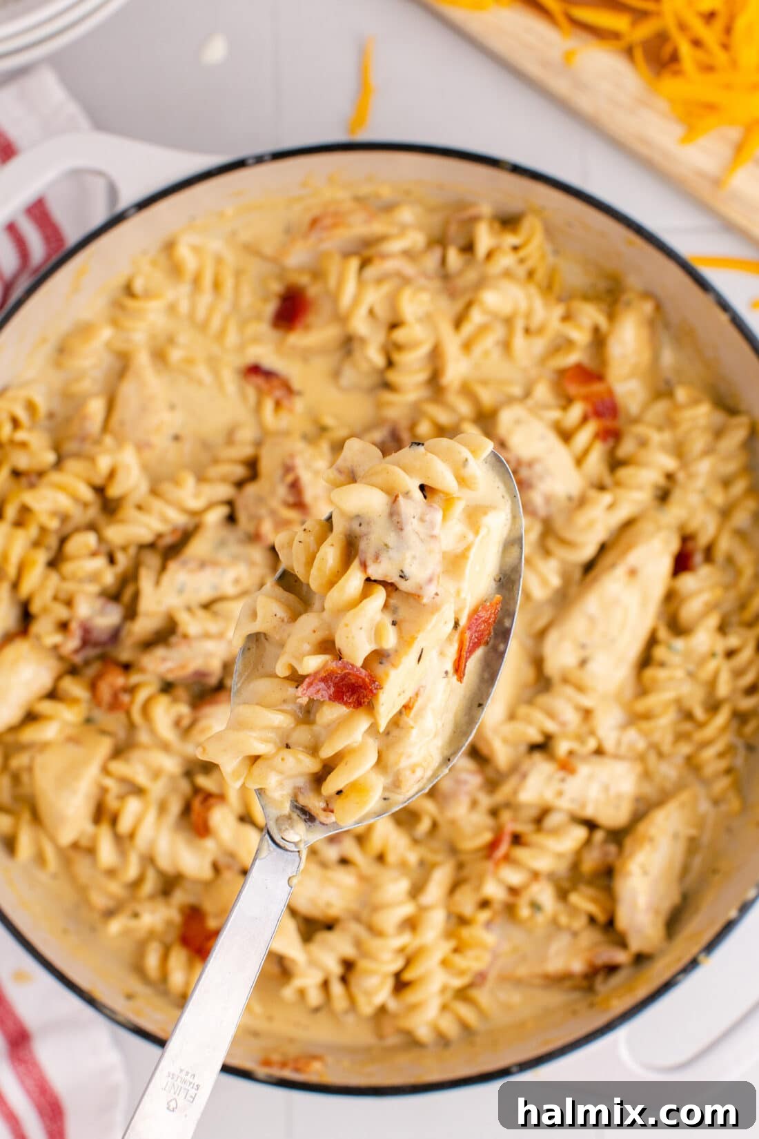 Spoonful of Creamy Chicken Bacon Ranch Pasta being lifted out of a pot, showcasing the rich sauce, tender chicken, and crispy bacon bits.