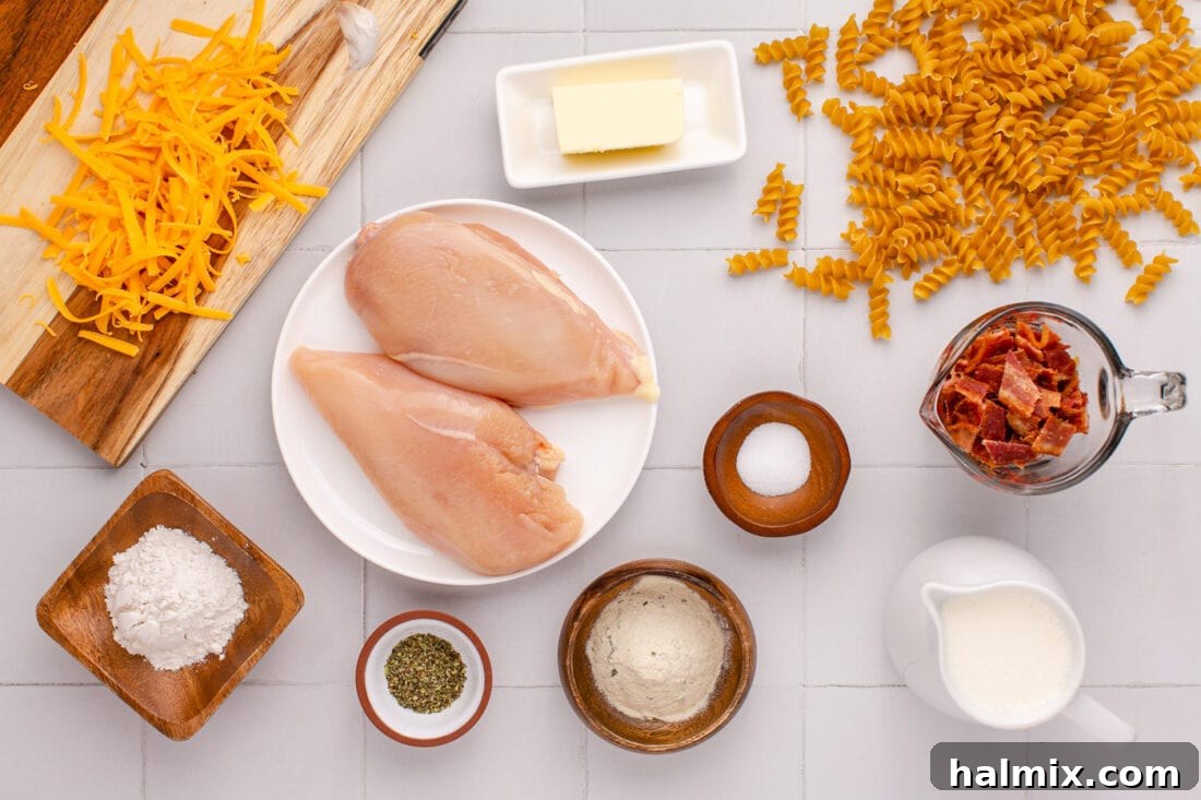All the fresh and prepared ingredients for making Creamy Chicken Bacon Ranch Pasta laid out on a kitchen surface.