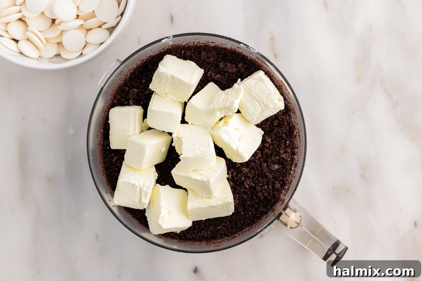 adding cream cheese cubes to food processor with oreos
