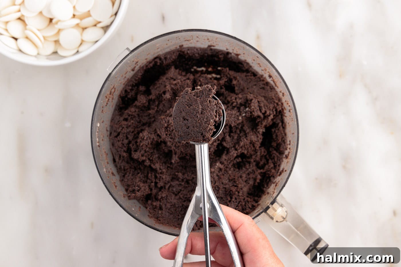 scooping out oreo dough from food processor onto a parchment-lined baking sheet