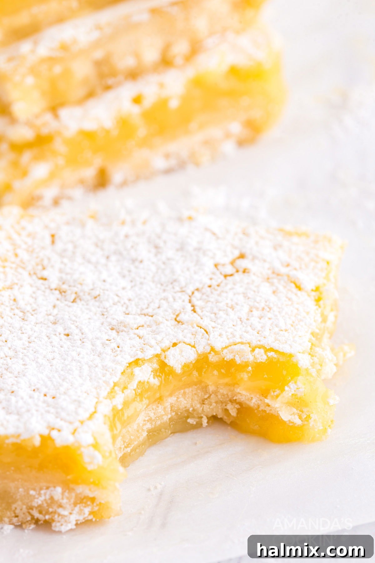 A perfectly baked lemon bar with a small bite taken out, revealing the vibrant yellow filling and the crisp crust beneath. It's garnished with a delicate dusting of powdered sugar, hinting at its irresistible flavor.