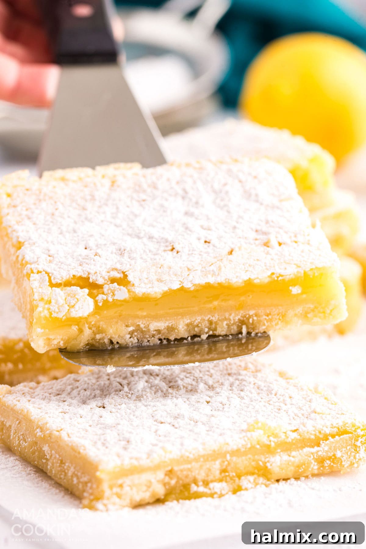 A delicate lemon bar being carefully lifted from the baking pan with a spatula, showcasing its crisp bottom crust and smooth, powdered sugar-dusted top. The rich yellow color of the filling is visible.
