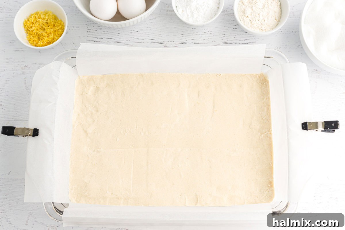 The shortbread mixture evenly patted down into a smooth, compact crust across the bottom of a baking pan, ready for the oven.