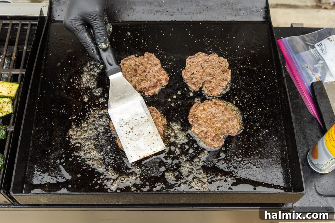 Spatula flattening burger patties again on a griddle after flipping