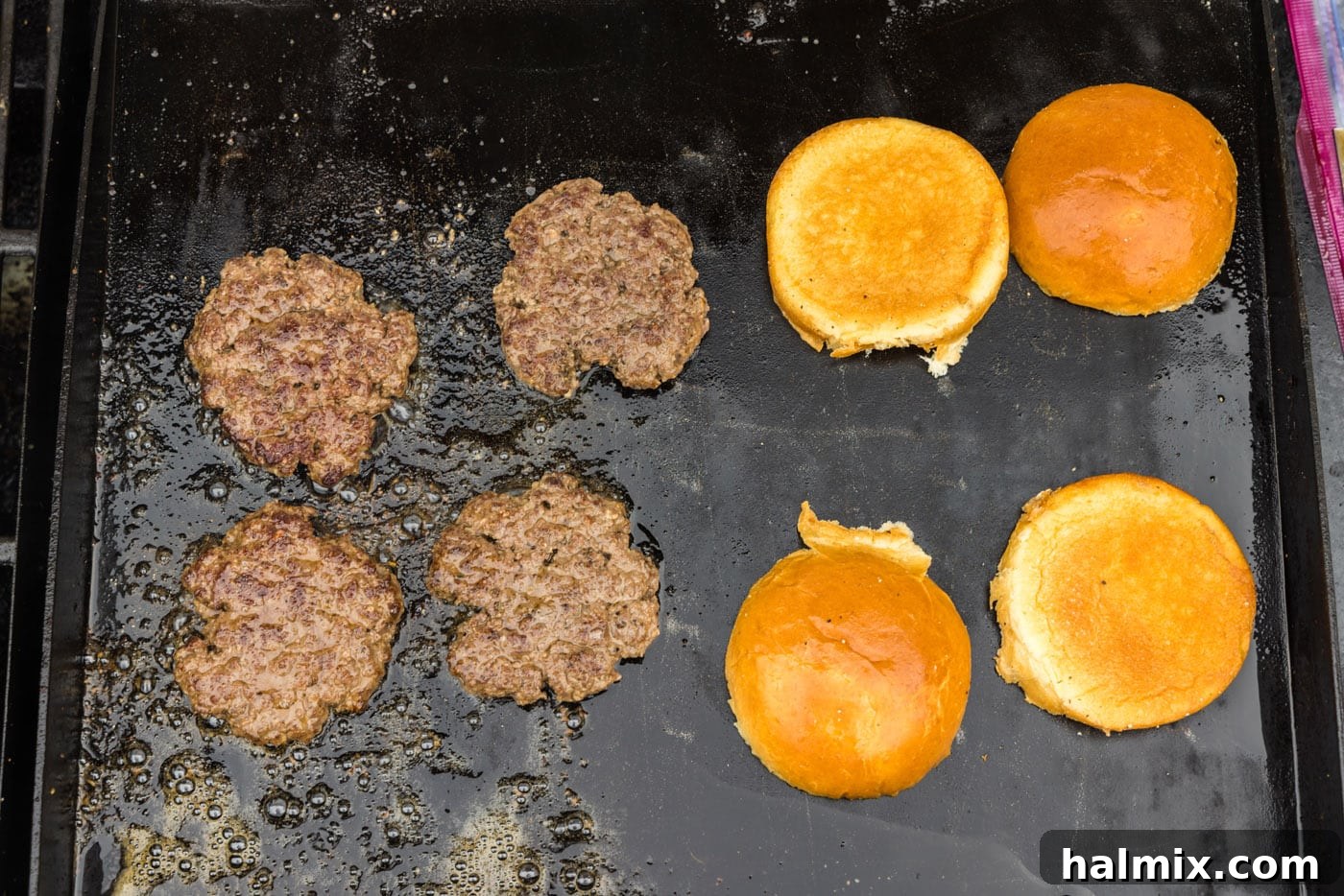 Hamburger buns and burger patties cooking on a griddle