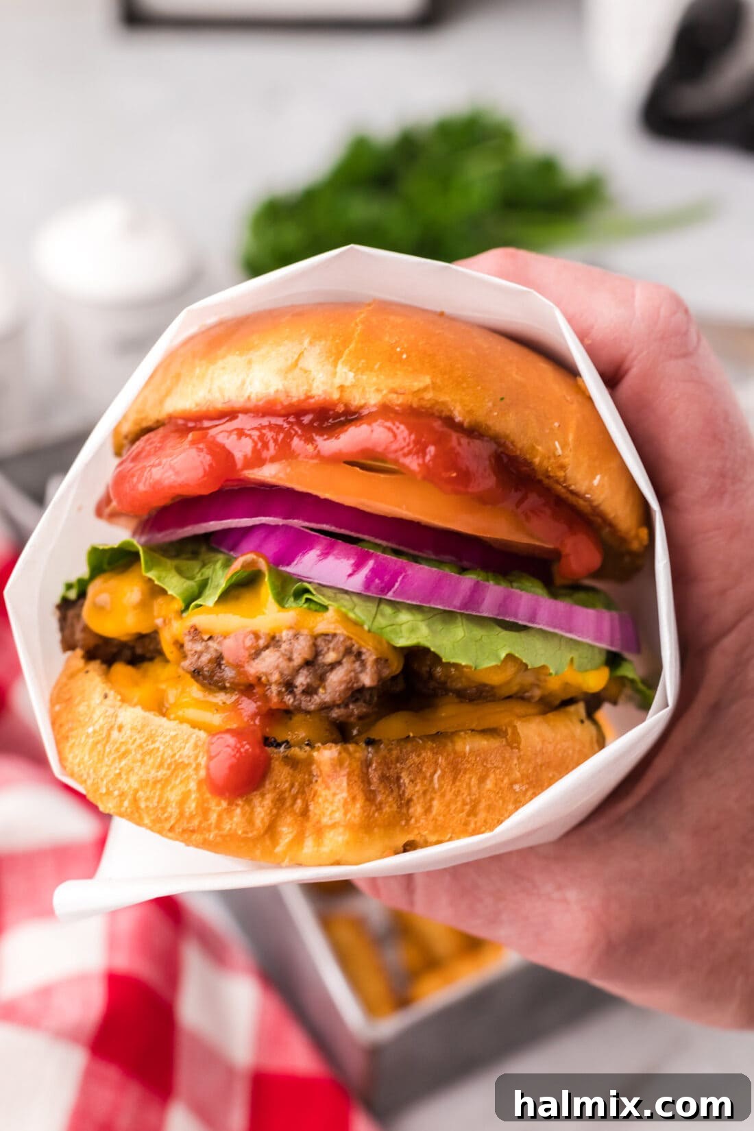 Hand holding a Smash Burger wrapped in parchment paper, ready to eat