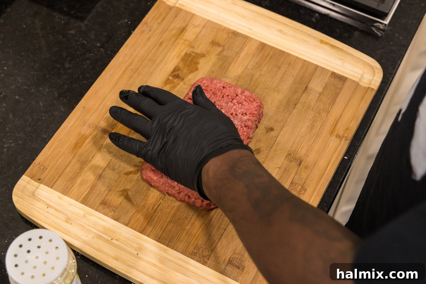 Hand pressing down on ground beef to flatten it for seasoning