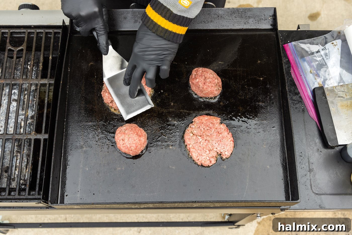 Pressing down on burger patties on a hot griddle with a spatula
