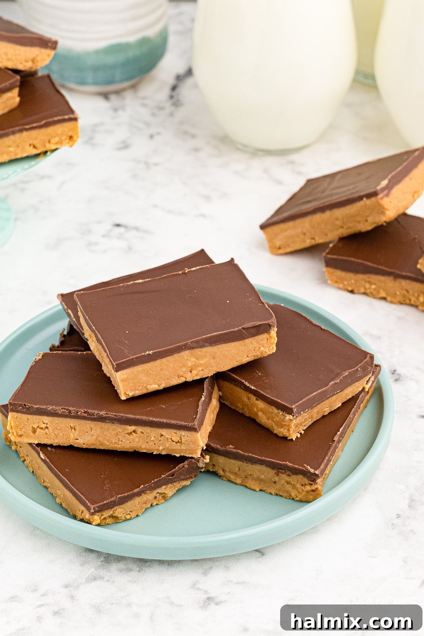 Delicious no-bake peanut butter bars stacked on a white plate, showcasing their chocolate topping and golden peanut butter base.