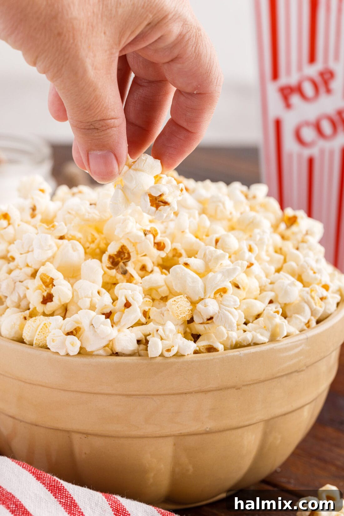 Hand grabbing Kettle Corn out of a bowl of Kettle Corn, highlighting the crispy texture