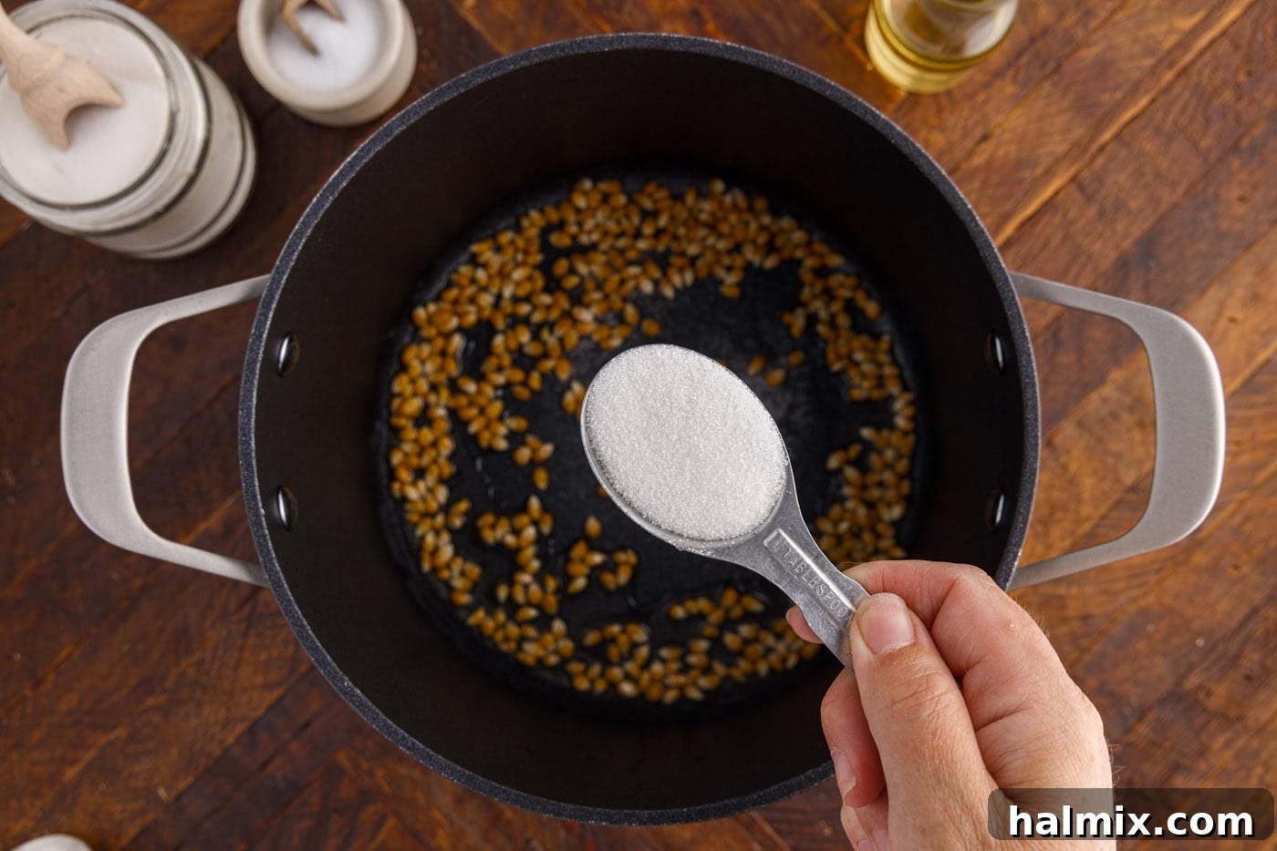 Sprinkling granulated sugar over popcorn kernels in a pot