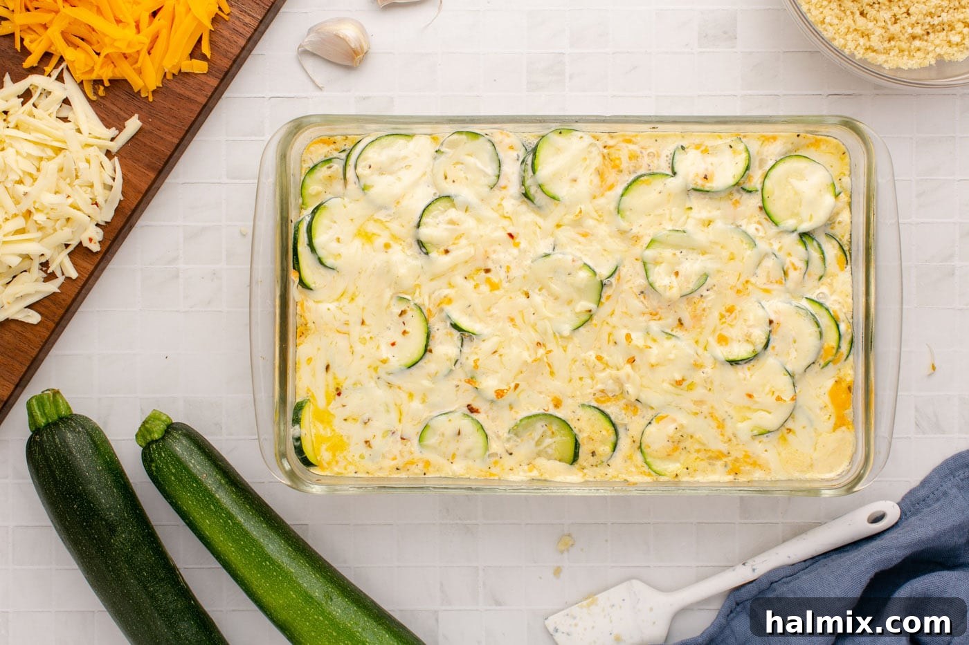 The zucchini casserole baking in the oven, covered with foil, allowing the cheese and vegetables to melt and tenderize.
