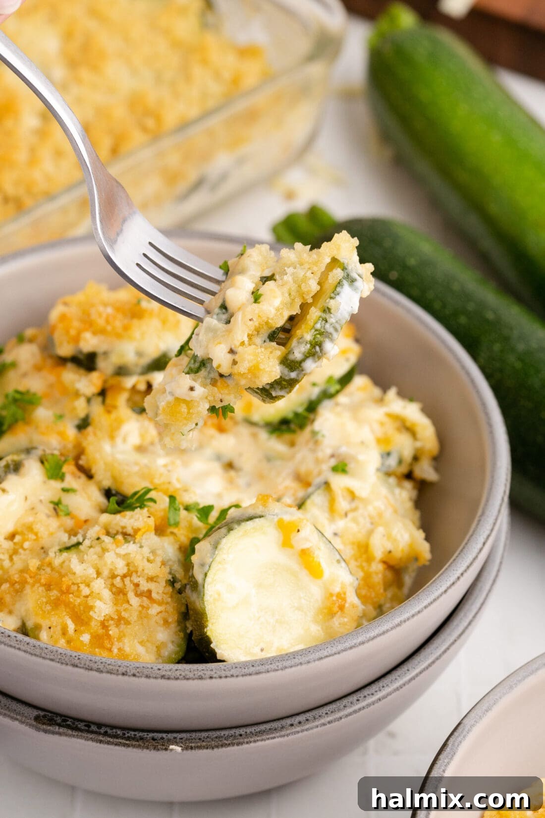 A fork lifts a creamy bite of Zucchini Casserole from a serving bowl, highlighting the perfectly melted cheese and tender squash.