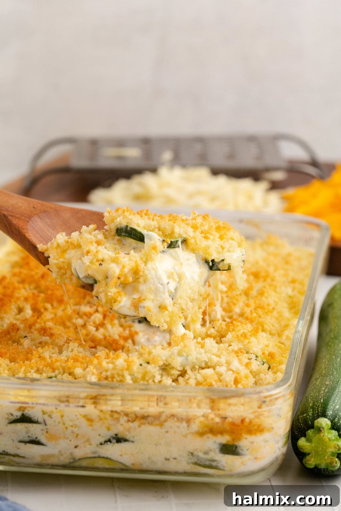 A spoonful of Zucchini Casserole is lifted from the baking dish, showing off the melted cheese and tender zucchini beneath the crisp panko topping.