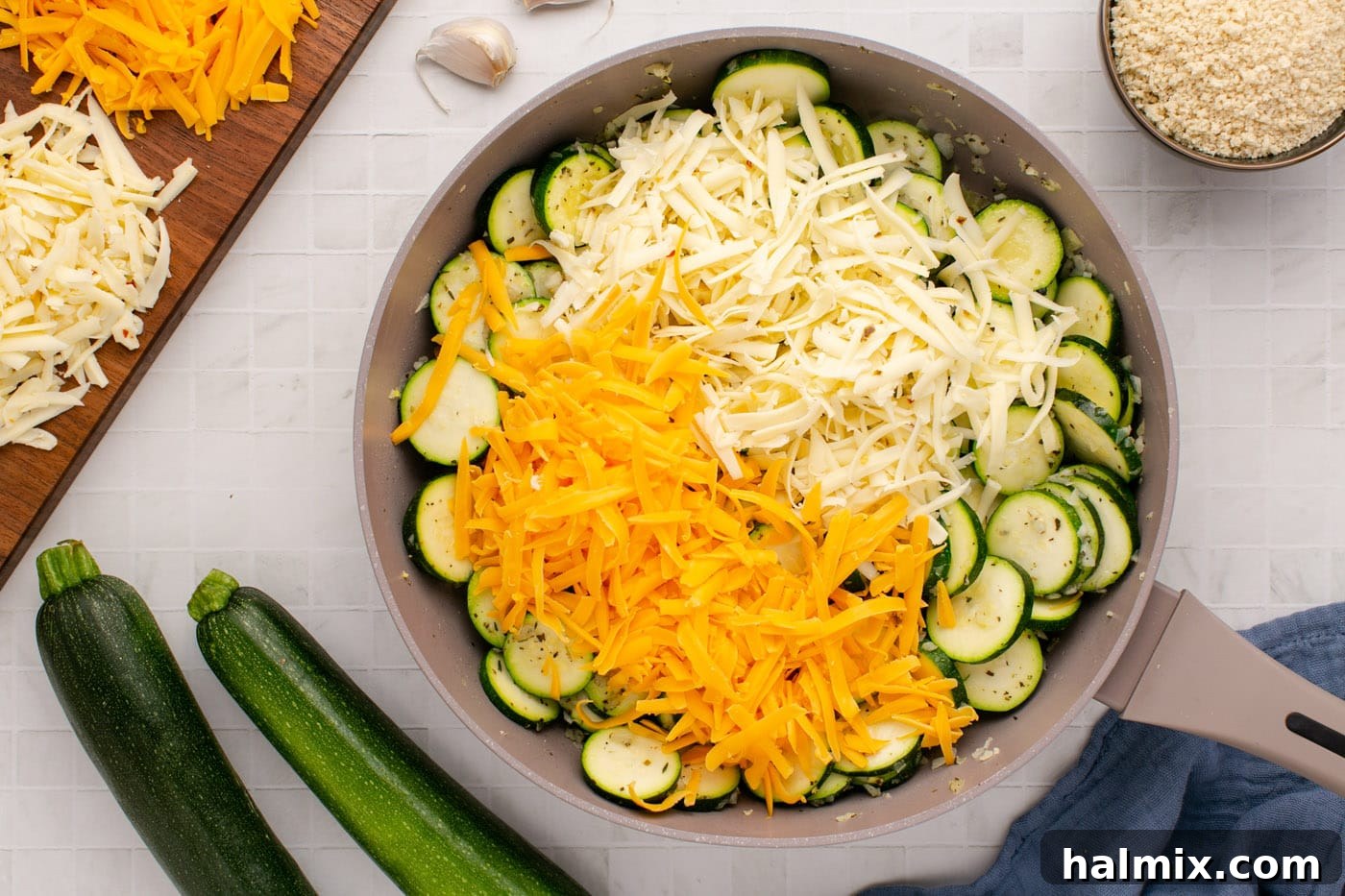 A generous amount of shredded cheddar and Monterey Jack cheese being added to the sautéed zucchini and onion mixture in the skillet.