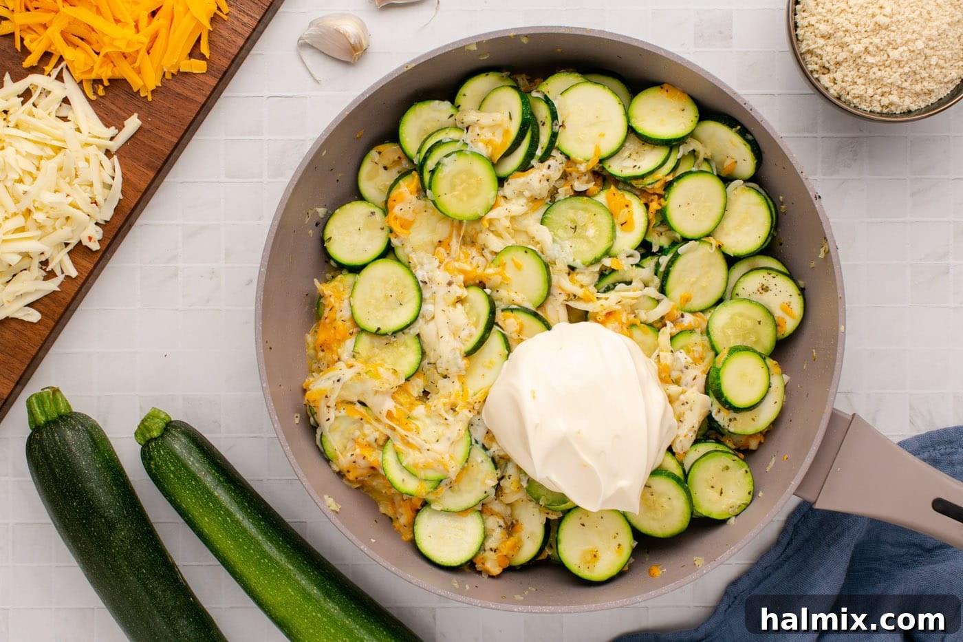 Creamy mayonnaise being stirred into the warm, cheesy zucchini mixture in the skillet, creating a rich and smooth consistency.