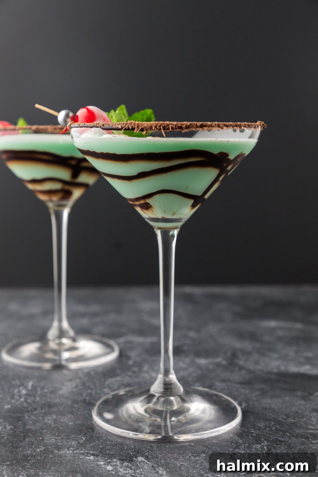 Two vibrant green Grasshopper cocktails in martini glasses, garnished with chocolate shavings and a maraschino cherry.