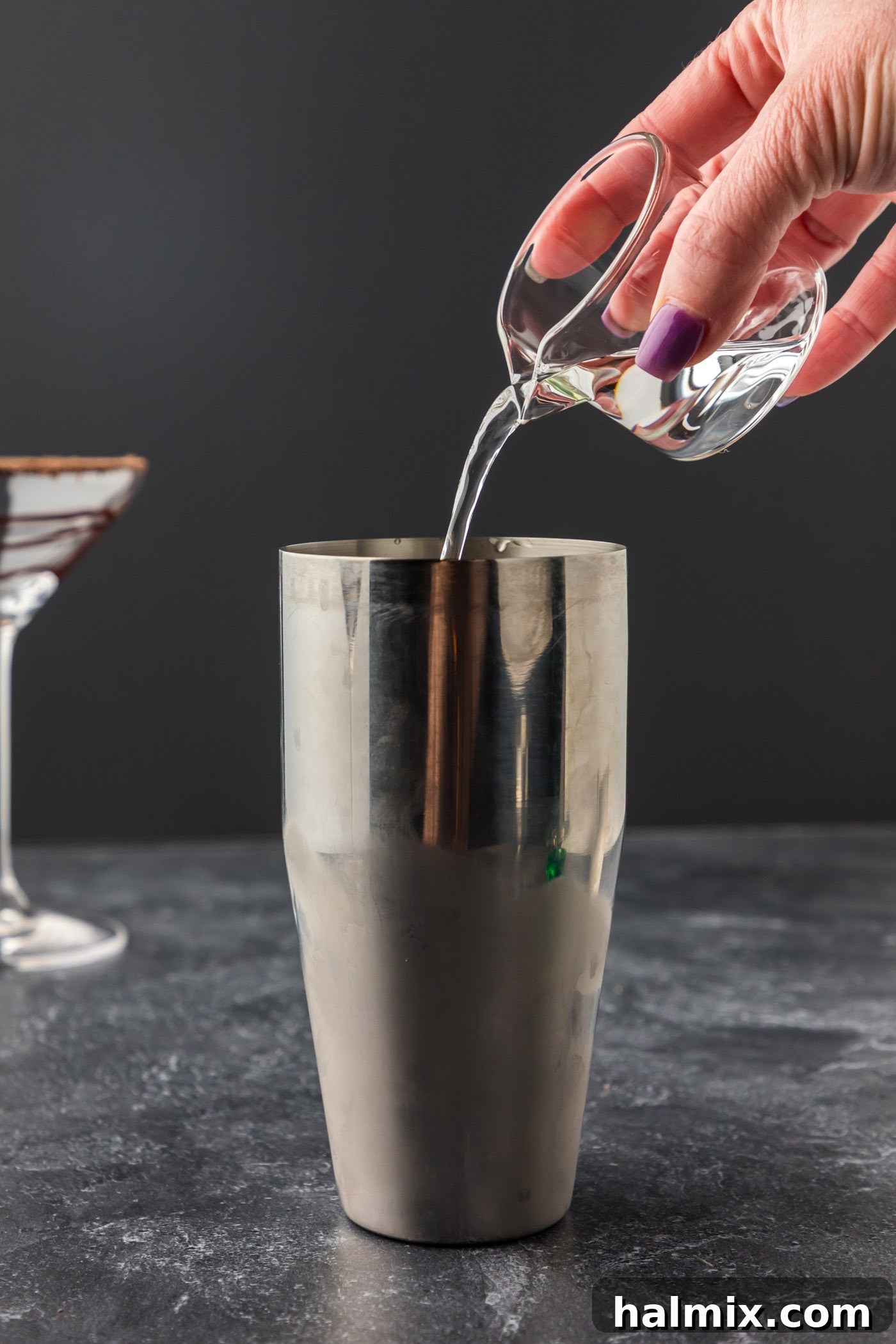 Pouring crème de cacao into a cocktail shaker filled with ice for a Grasshopper drink.
