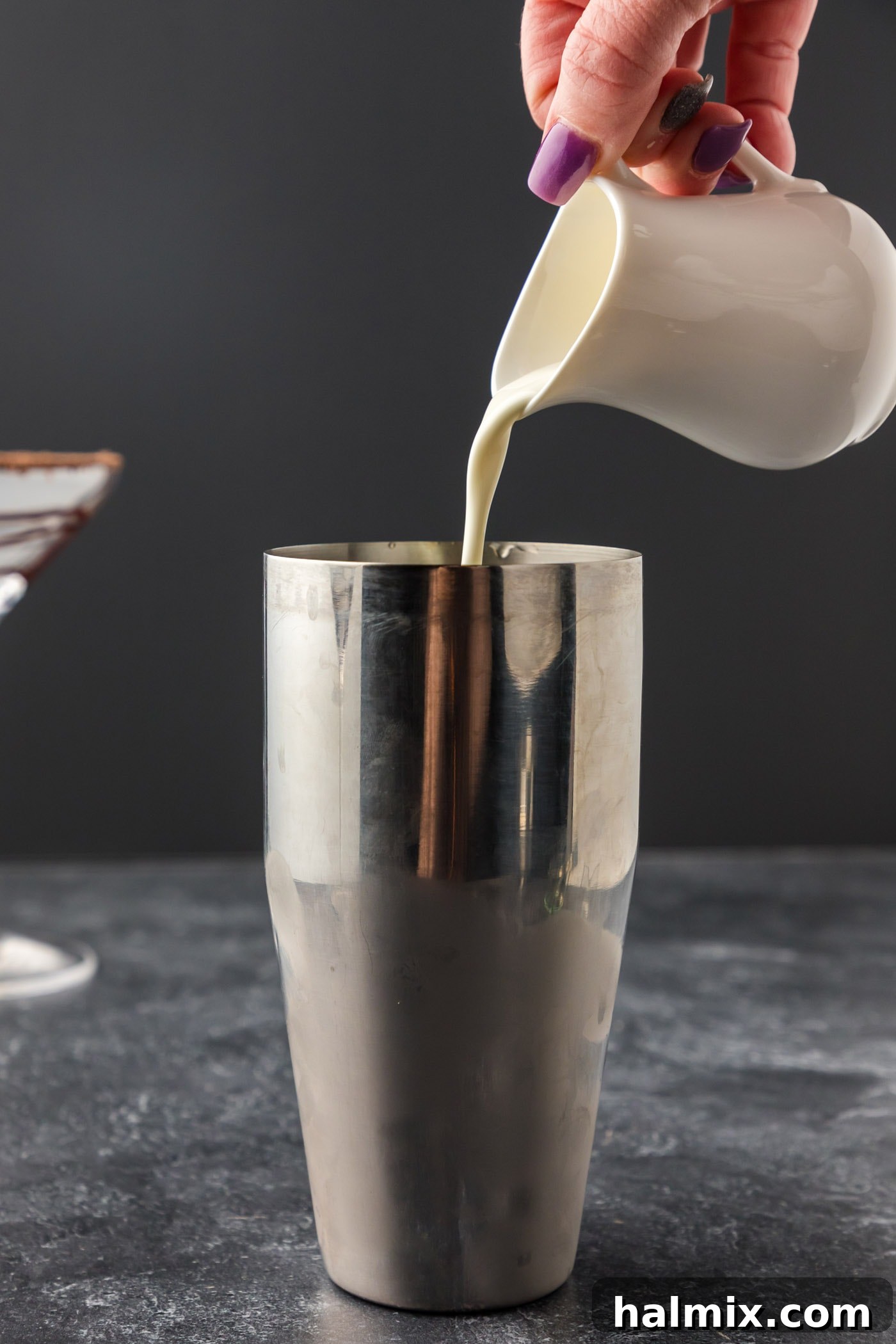 Pouring rich heavy cream into the cocktail shaker, completing the base ingredients for the creamy Grasshopper cocktail.