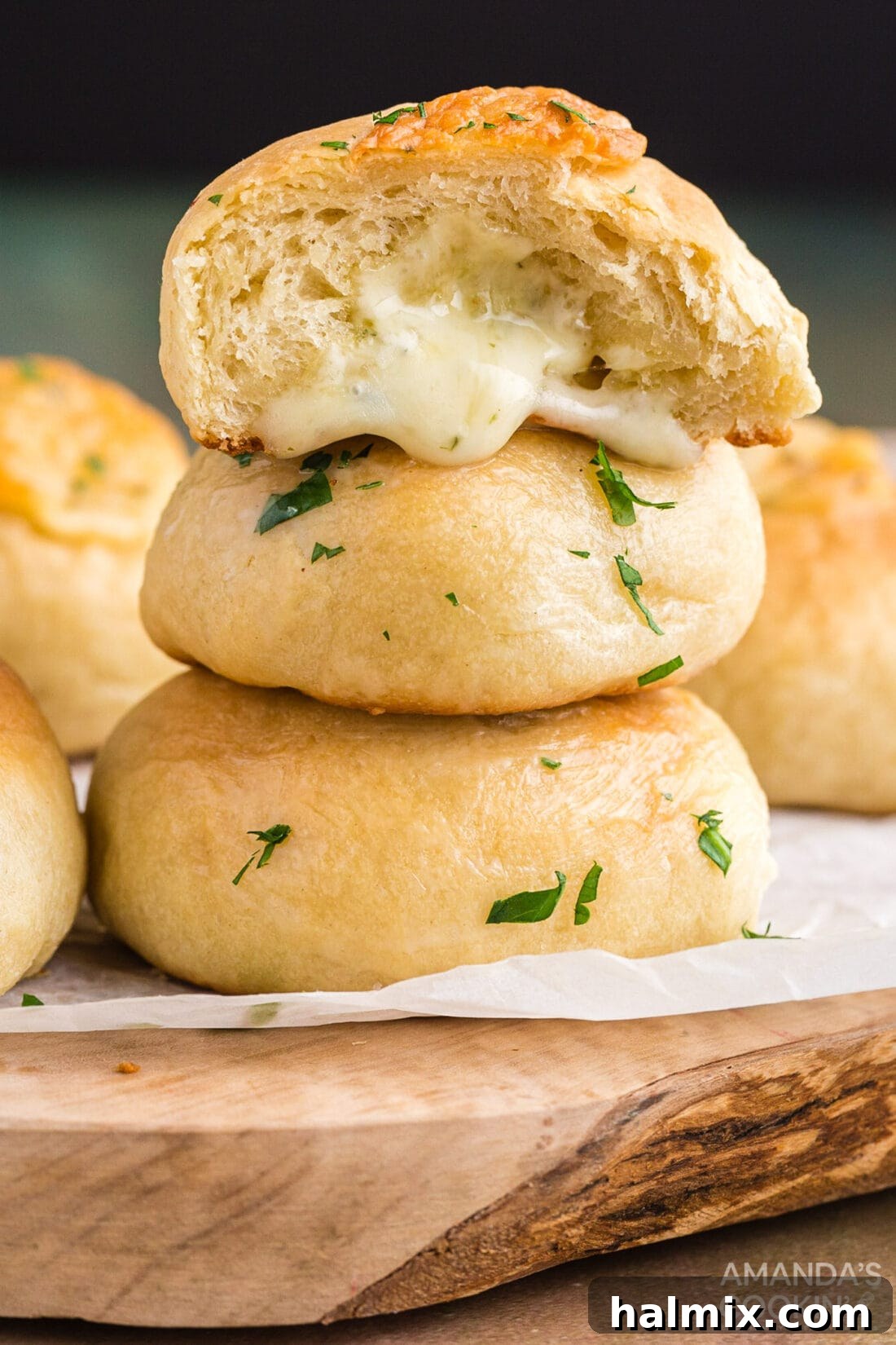Stacks of warm, golden-brown garlic cheese rolls on a wooden cutting board, ready to be served.