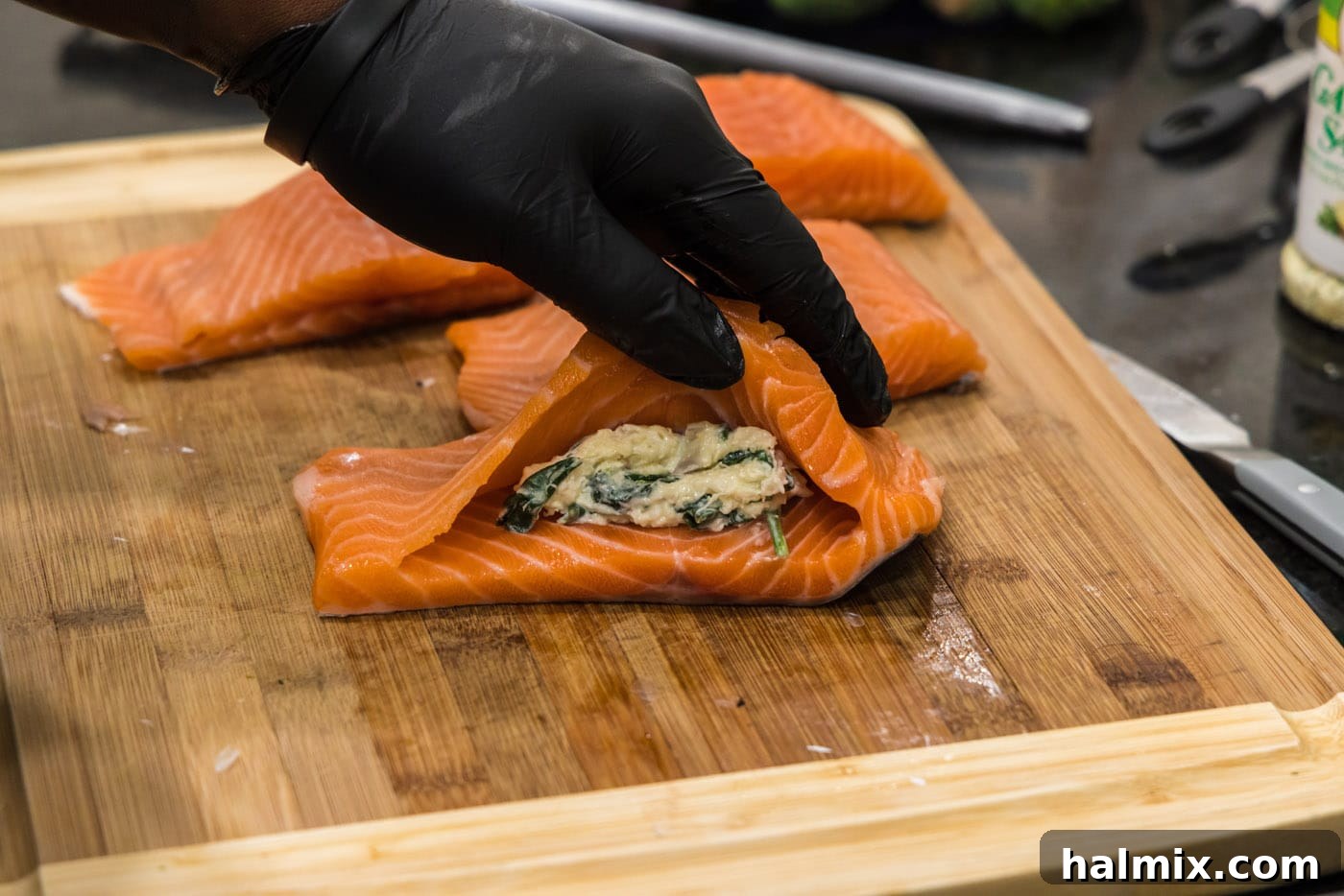 Adding spoonfuls of creamy crab and spinach stuffing into the prepared pocket of a salmon fillet.