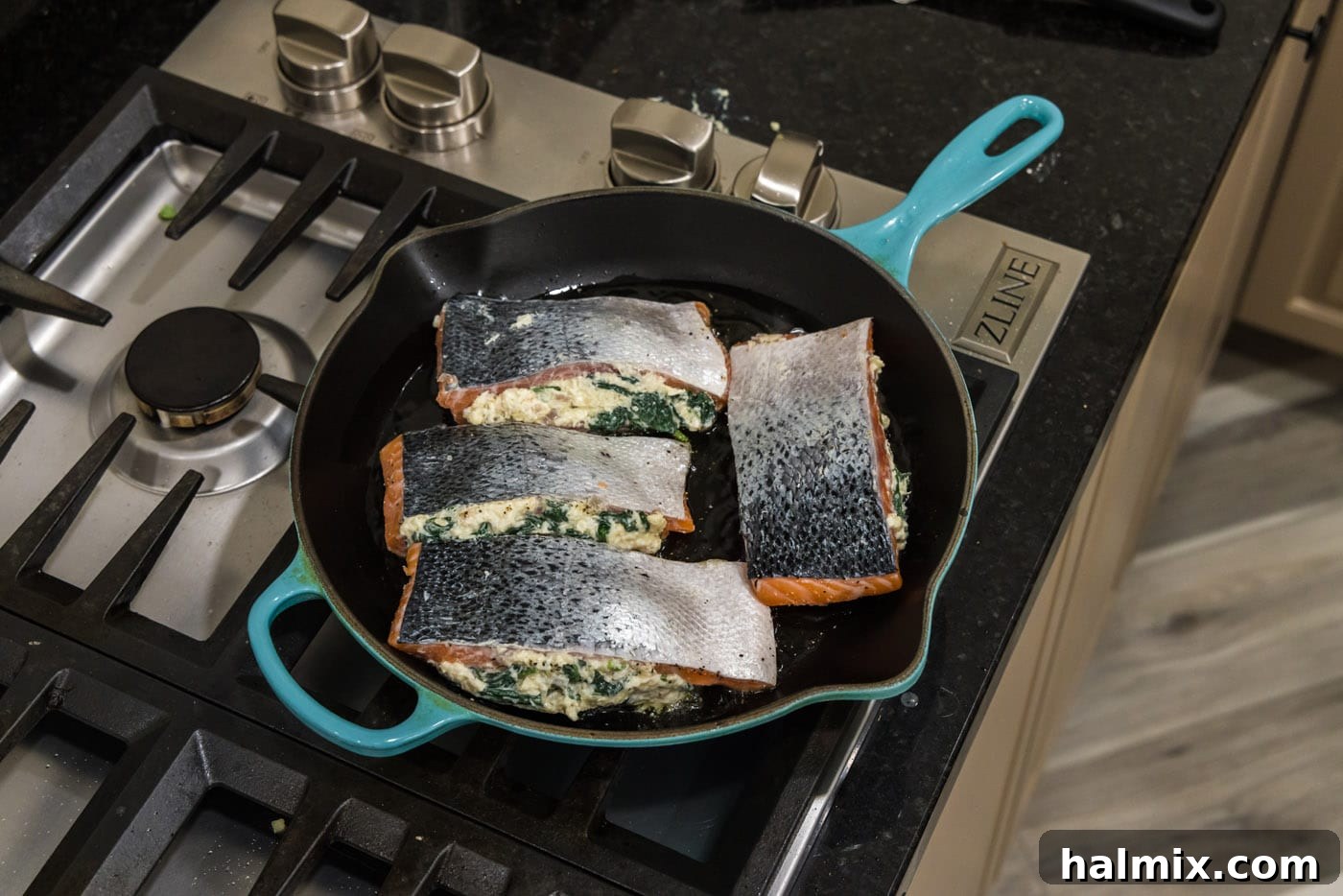Searing stuffed salmon fillets flesh-side down in a hot skillet, creating a perfect golden crust.