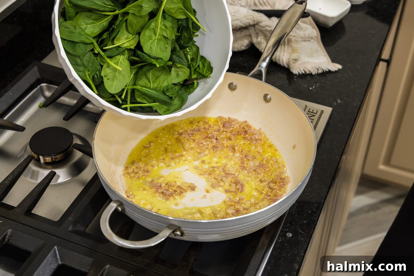 Fresh spinach leaves being added to the skillet with sautéed shallots and garlic, ready to wilt down.