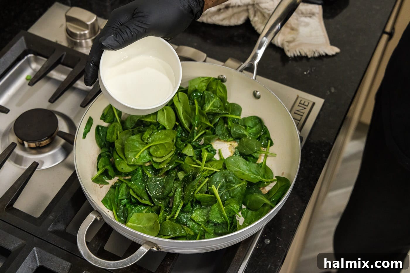 Pouring heavy cream into the skillet containing wilted spinach, shallots, and garlic to create a creamy base for the stuffing.