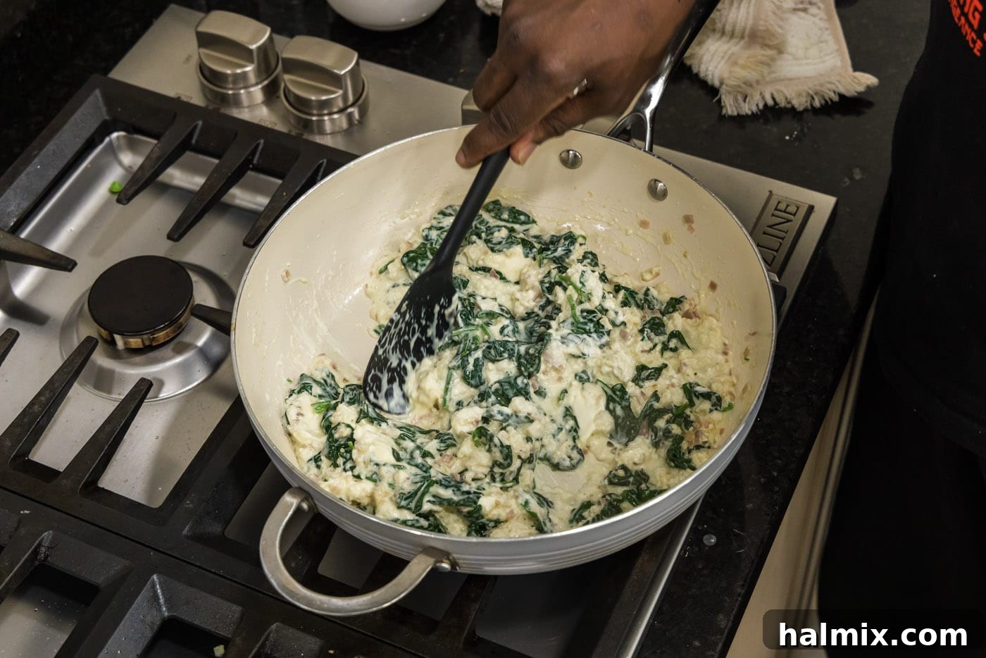 Stirring the cream cheese, spinach, and crab mixture in a skillet until everything is combined and creamy.