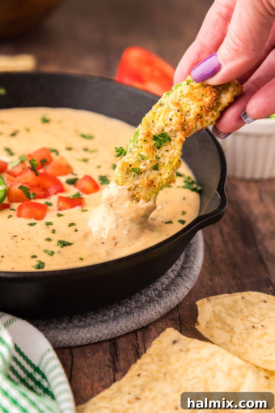 An air fryer avocado fry being dipped into a skillet of Queso Dip