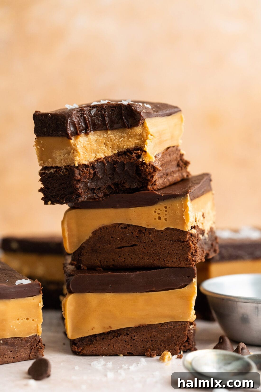 Stack of three Millionaire Brownies with a bite removed from the top one, showcasing the distinct layers of fudge brownie, caramel, and chocolate ganache.