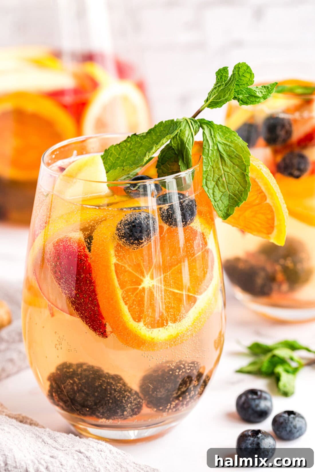 Sun-Kissed Sangria 2 Close up photo of a glass of white moscato sangria, garnished with fresh fruit and mint.