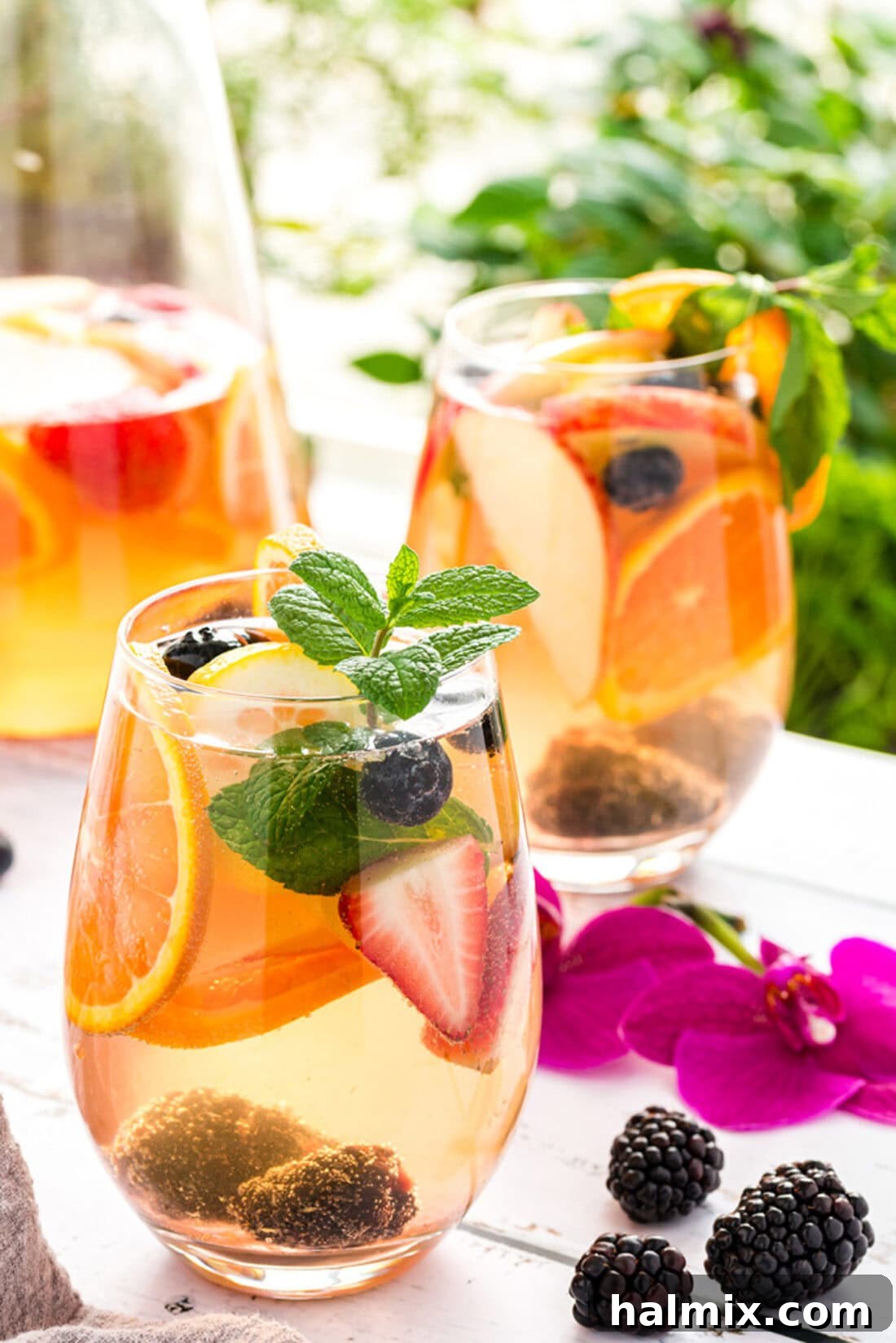 Sun-Kissed Sangria 6 Two glasses of white sangria, garnished with berries and citrus slices, on a wooden table.