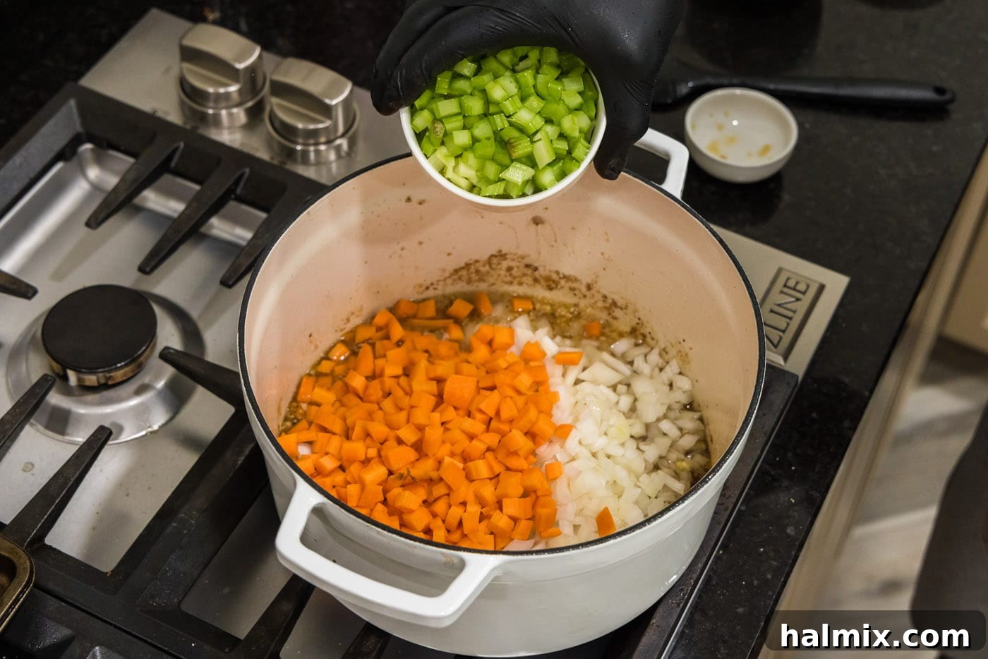 Adding celery to a pot with carrots, onion, and garlic in white wine