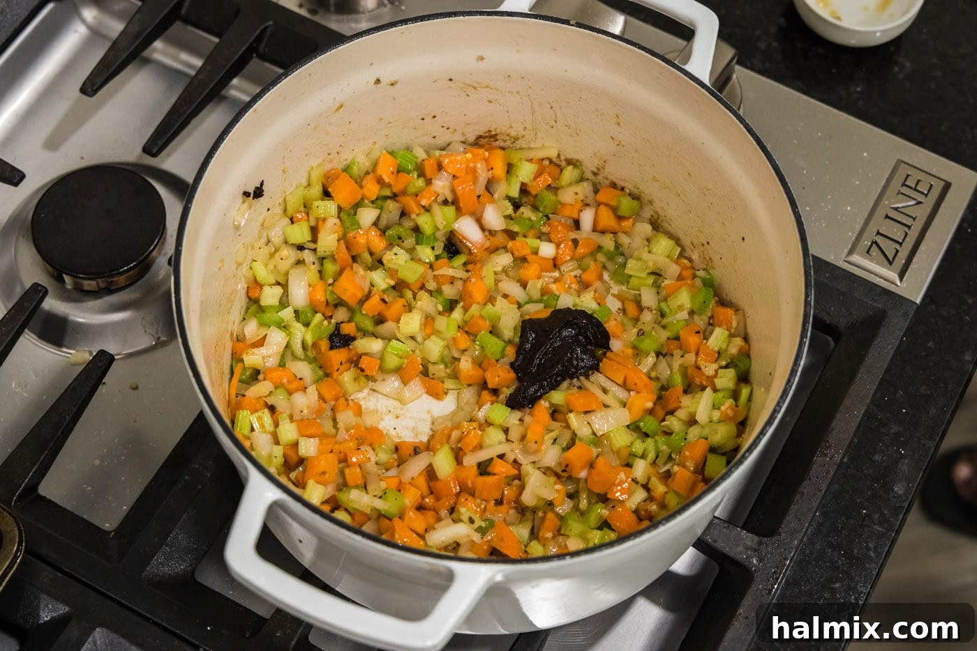 Beef base added to vegetables in the pot, stirring to combine