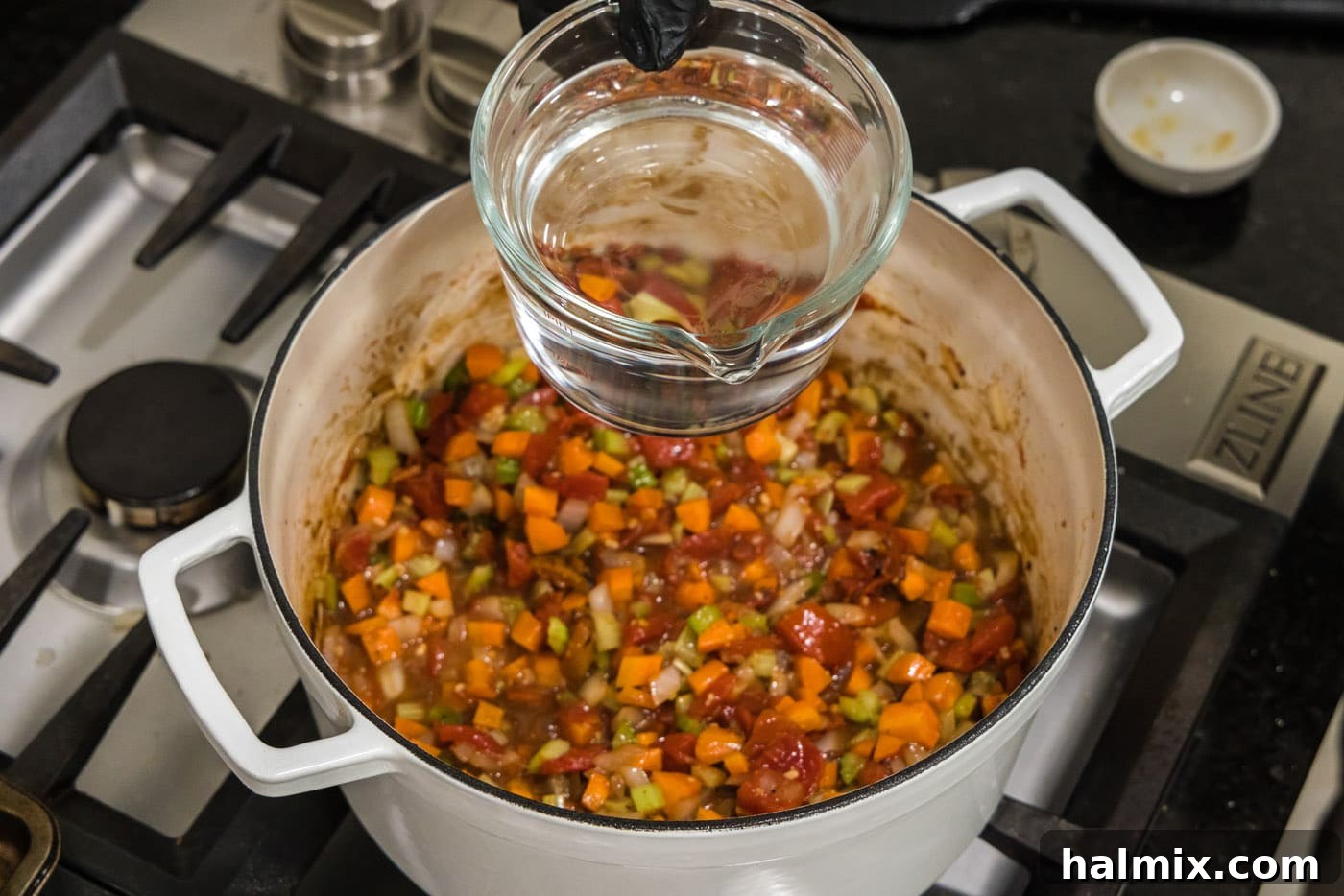 Pouring water into a Dutch oven with vegetables and sauce base