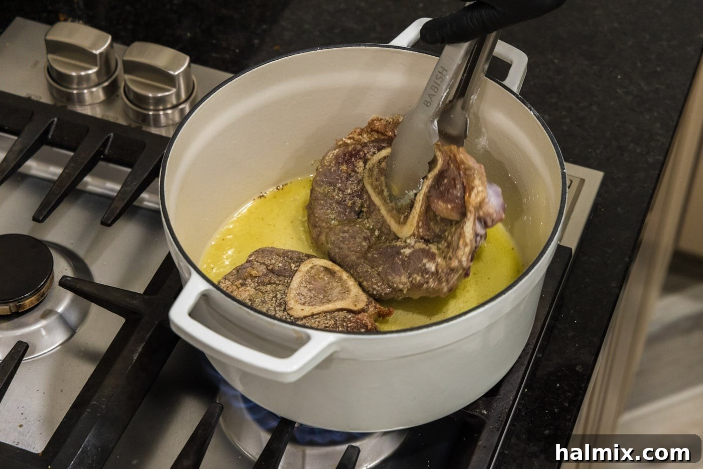 Tongs flipping beef shanks in a Dutch oven to brown both sides