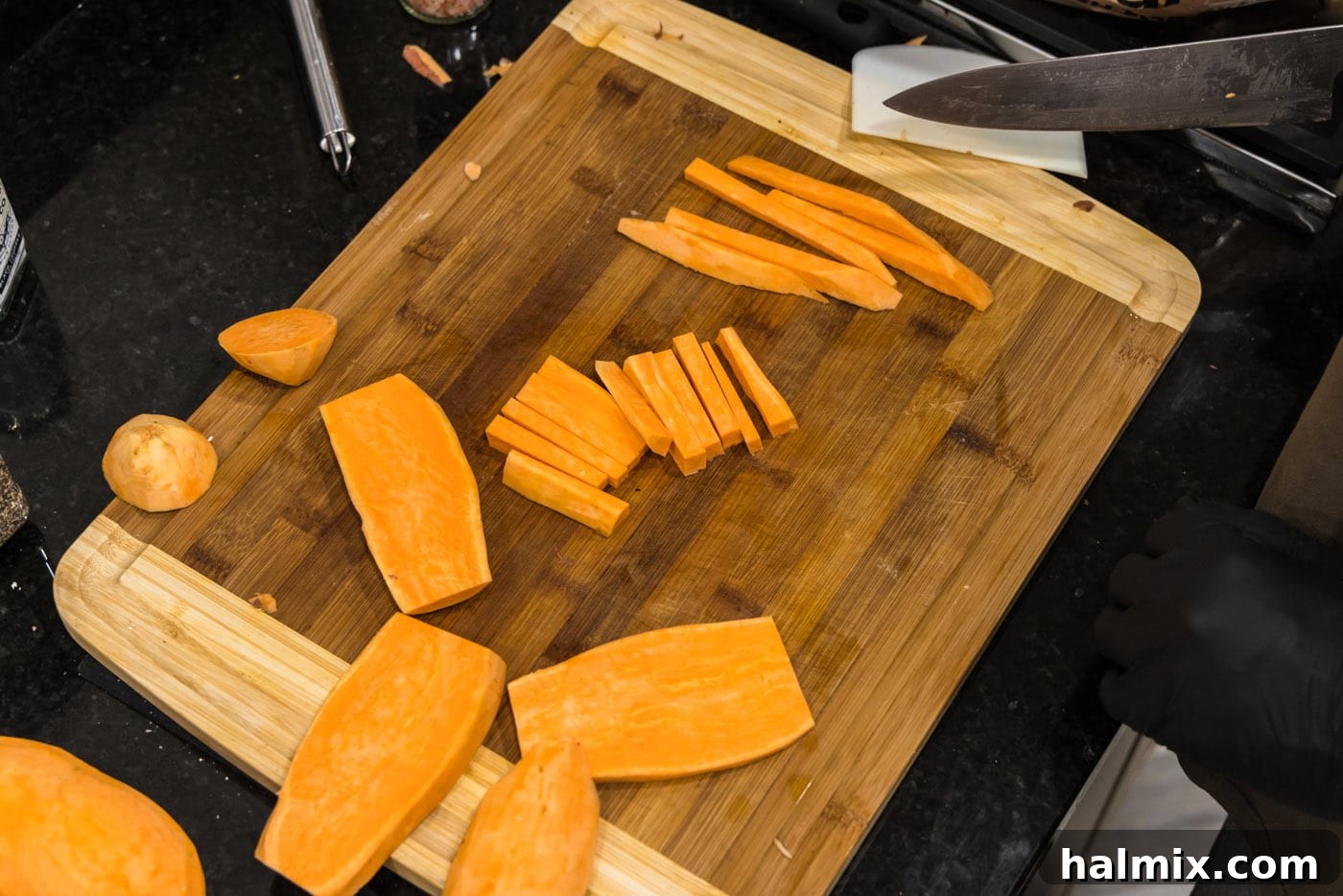 Slicing peeled sweet potatoes into uniform sticks on a cutting board.