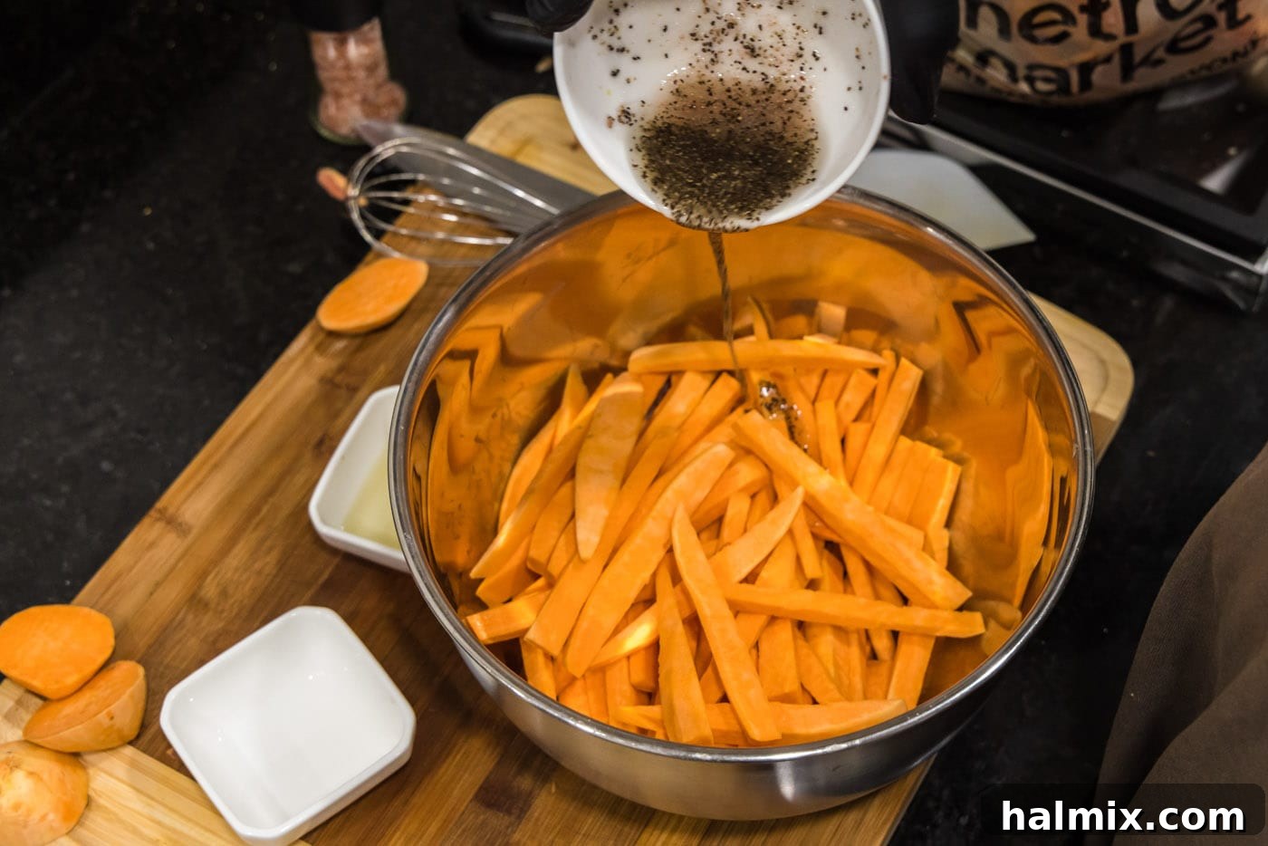Pouring the seasoned olive oil mixture over the sweet potato fries in a large bowl.