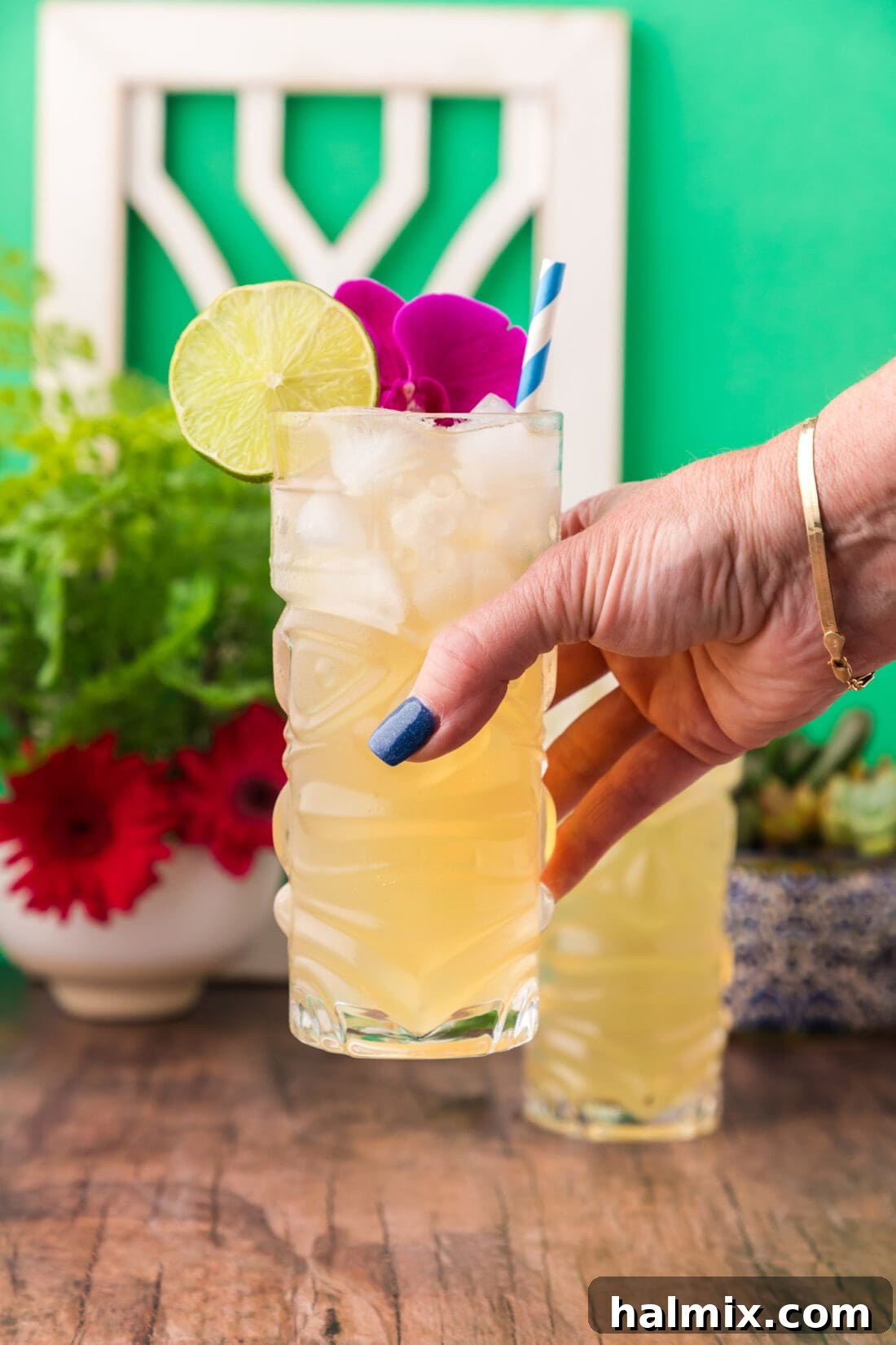 A hand holding a frosty glass of Jamaican Mule, garnished with a lime wedge, against a bright, sunny background, evoking a perfect tropical moment.